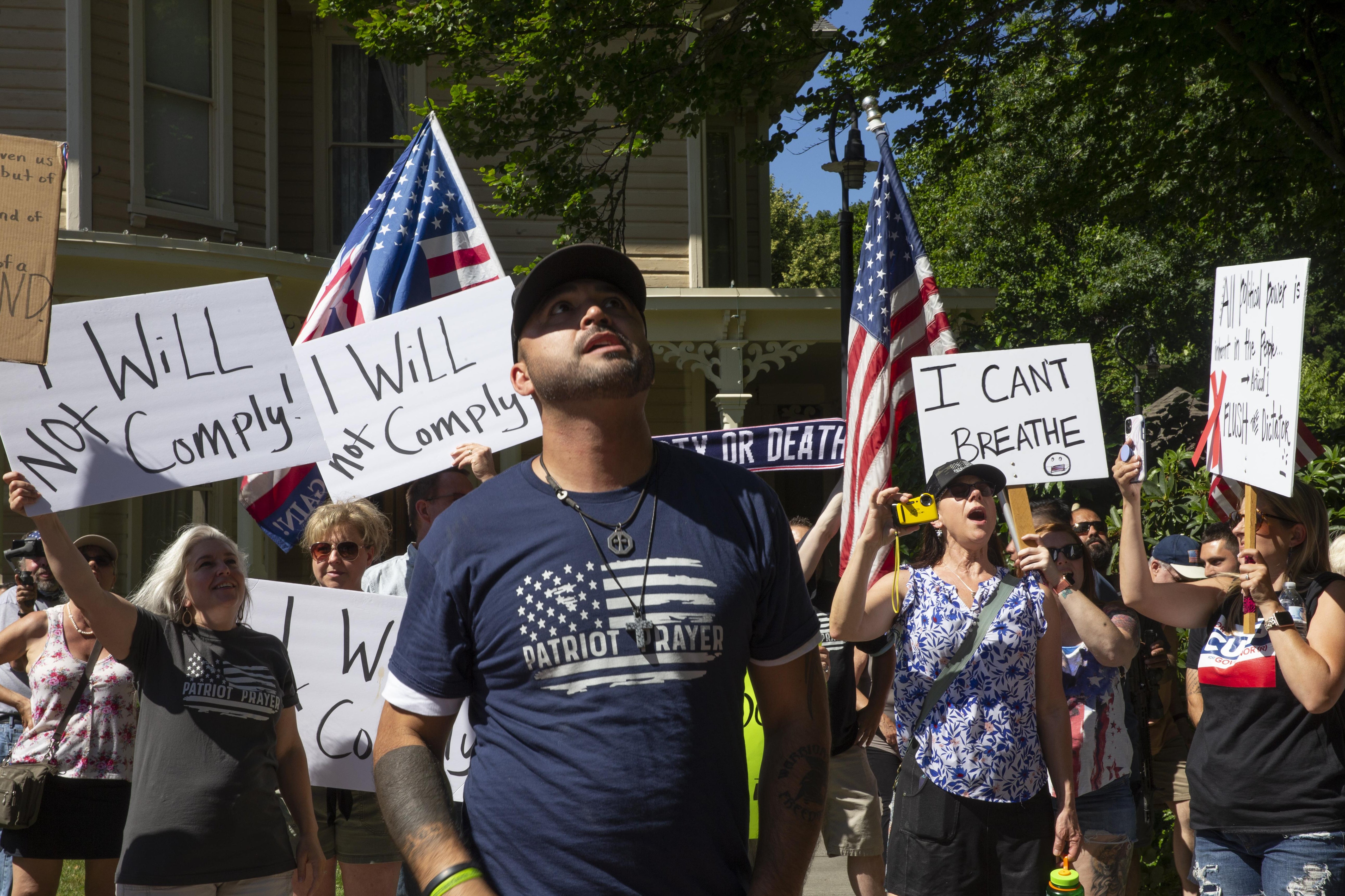 Joey Gibson standing in front of a crowd of people holding signs that say "I CAN'T BREATHE" and "I WILL NOT COMPLY"