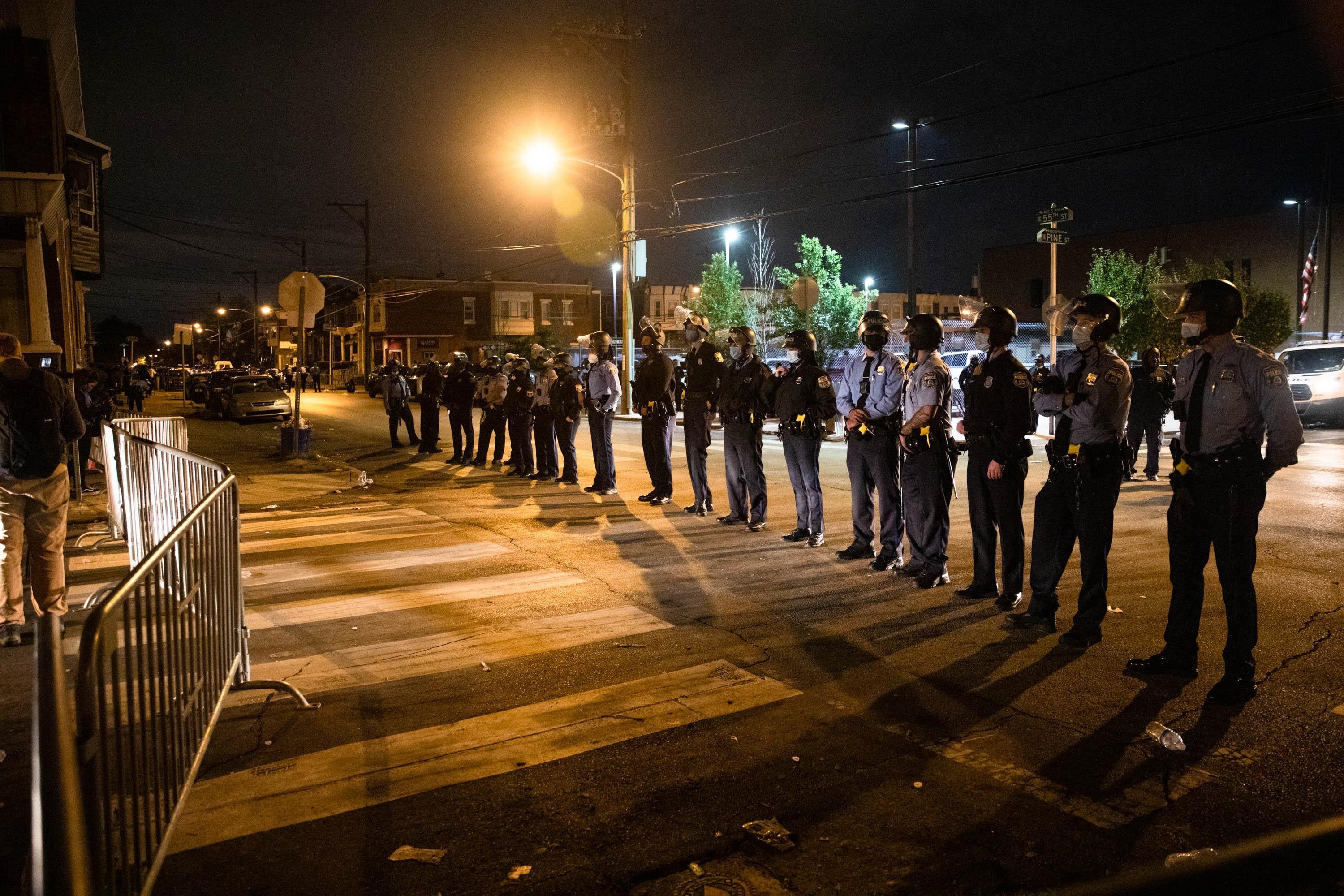 A line of police officers in masks behind a barrier at night.
