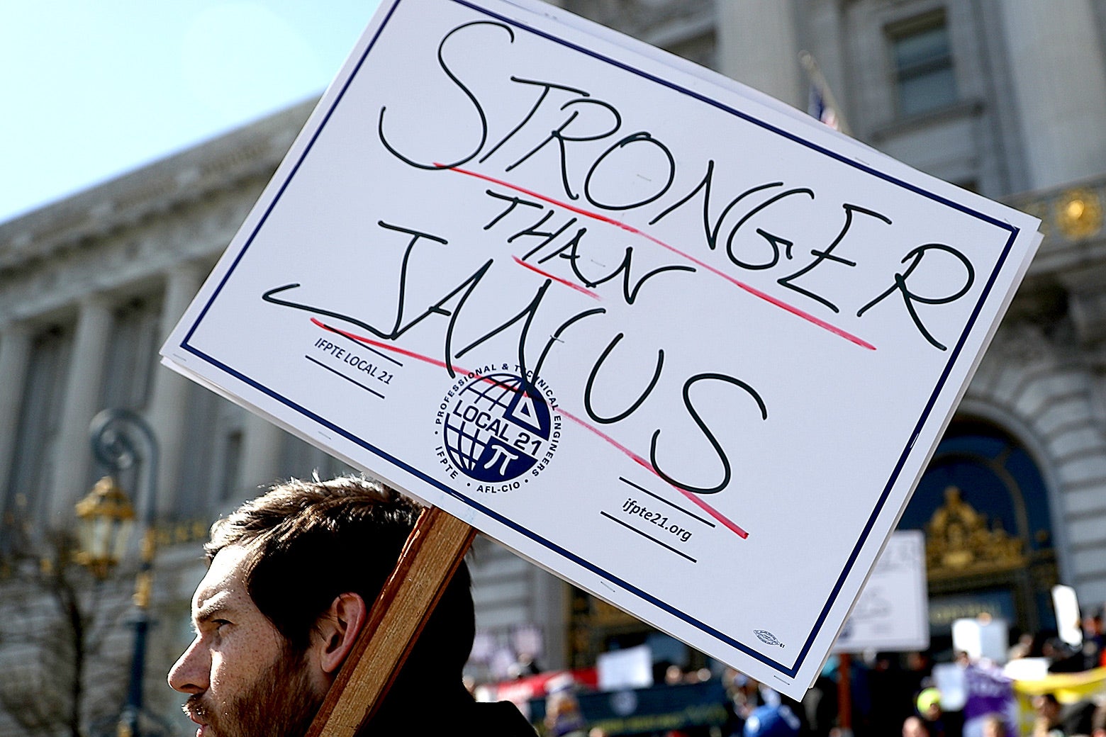 A union member protesting outside San Francisco City Hall holds a sign reading "STRONGER THAN JANUS."