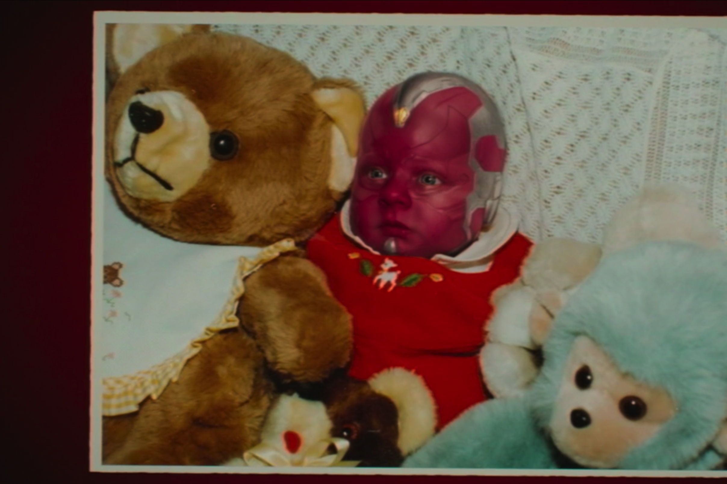 Baby Vision sits in a bed with some stuffed animals.