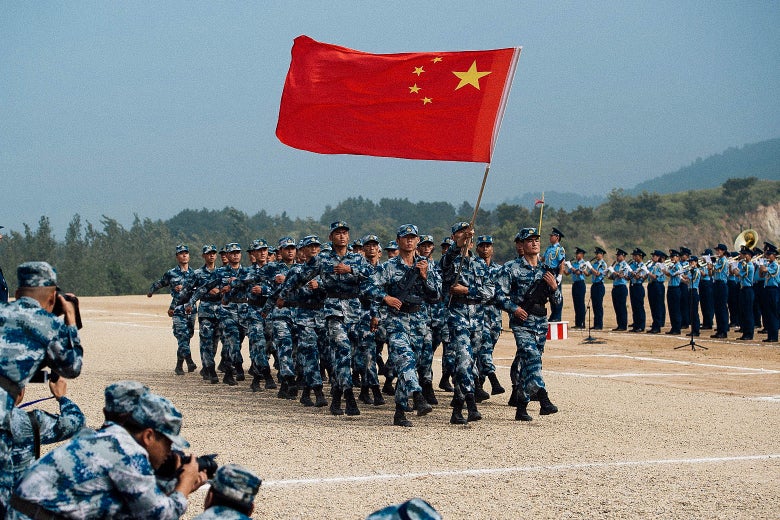 Uniformed Chinese troops march in formation with their national flag.