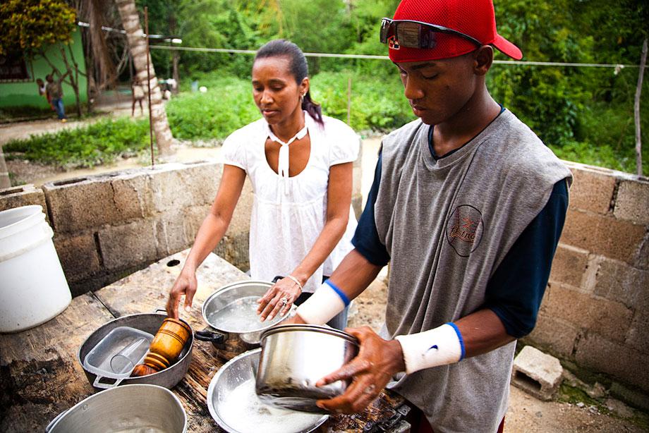 BOCA CHICA, DOMINICAN REPUBLIC. A portrait of a top prospect, Raymel Flores, who at this time was anxiously awaiting his 16.5 birthday when he was eligible to sign with an MLB team. His tiny home has a tin roof and leaks water throughout the year. Here, he washes dishes with his mother. A few weeks after this image was taken, Raymel signed with the Boston Red Sox for USD$900,000.