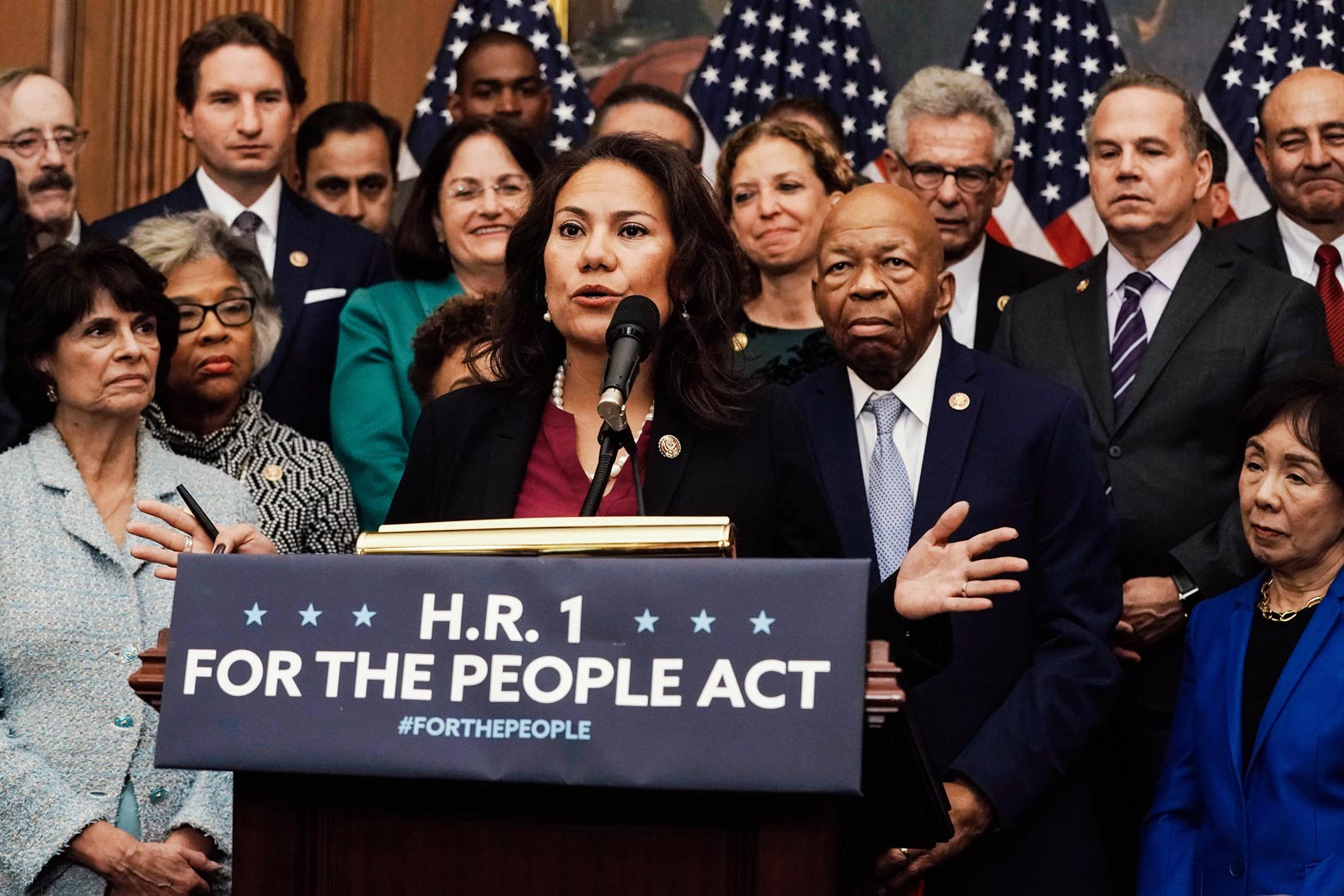 Veronica Escobar speaks from behind a podium that says, "H.R. 1: For the People Act," surrounded by colleagues.