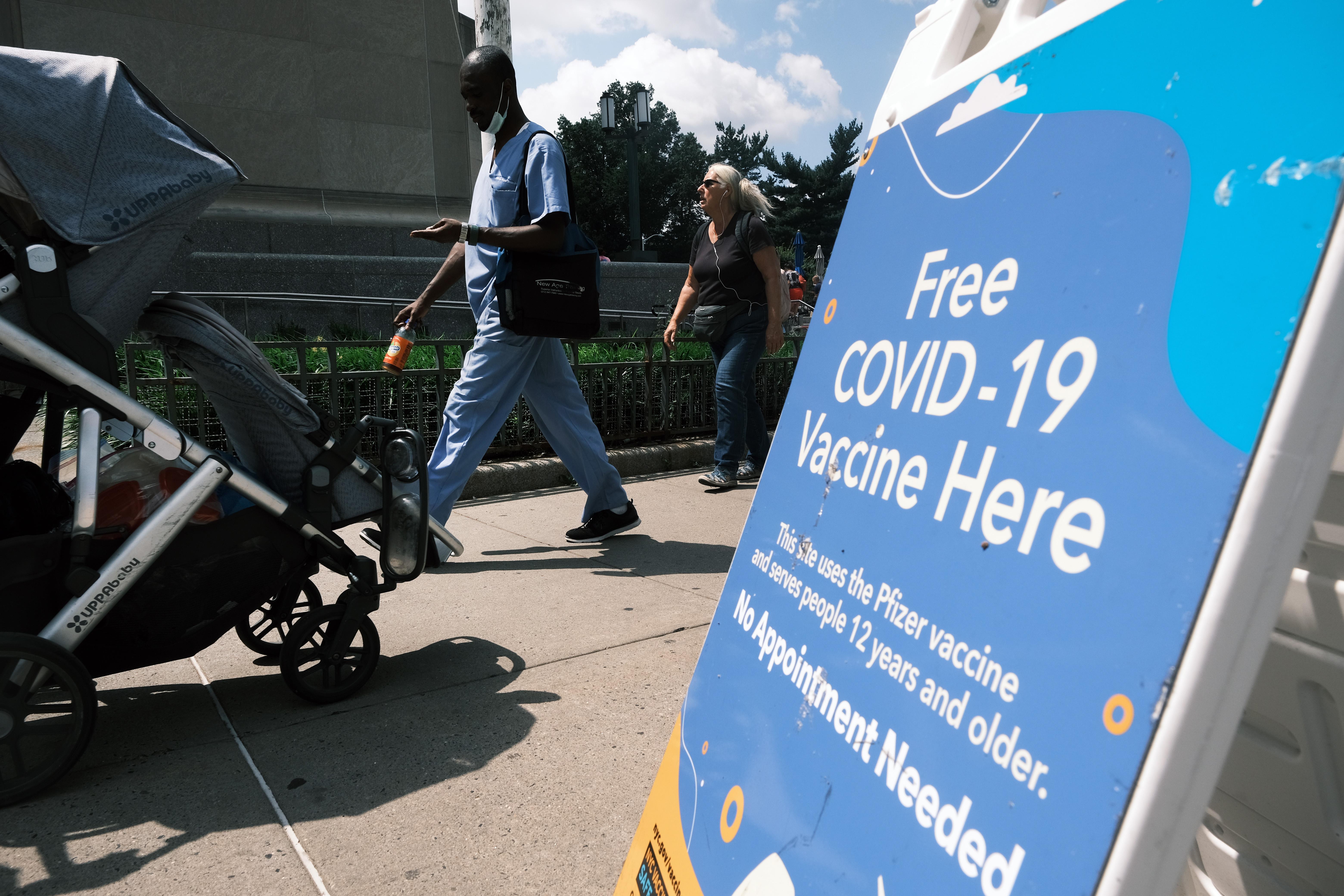 People walk by a sign that says "Free COVID-19 Vaccine Here."