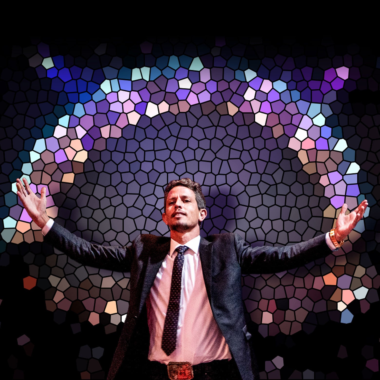 Tony Hinchcliffe has his hands raised standing in a spotlight in front of stained glass.