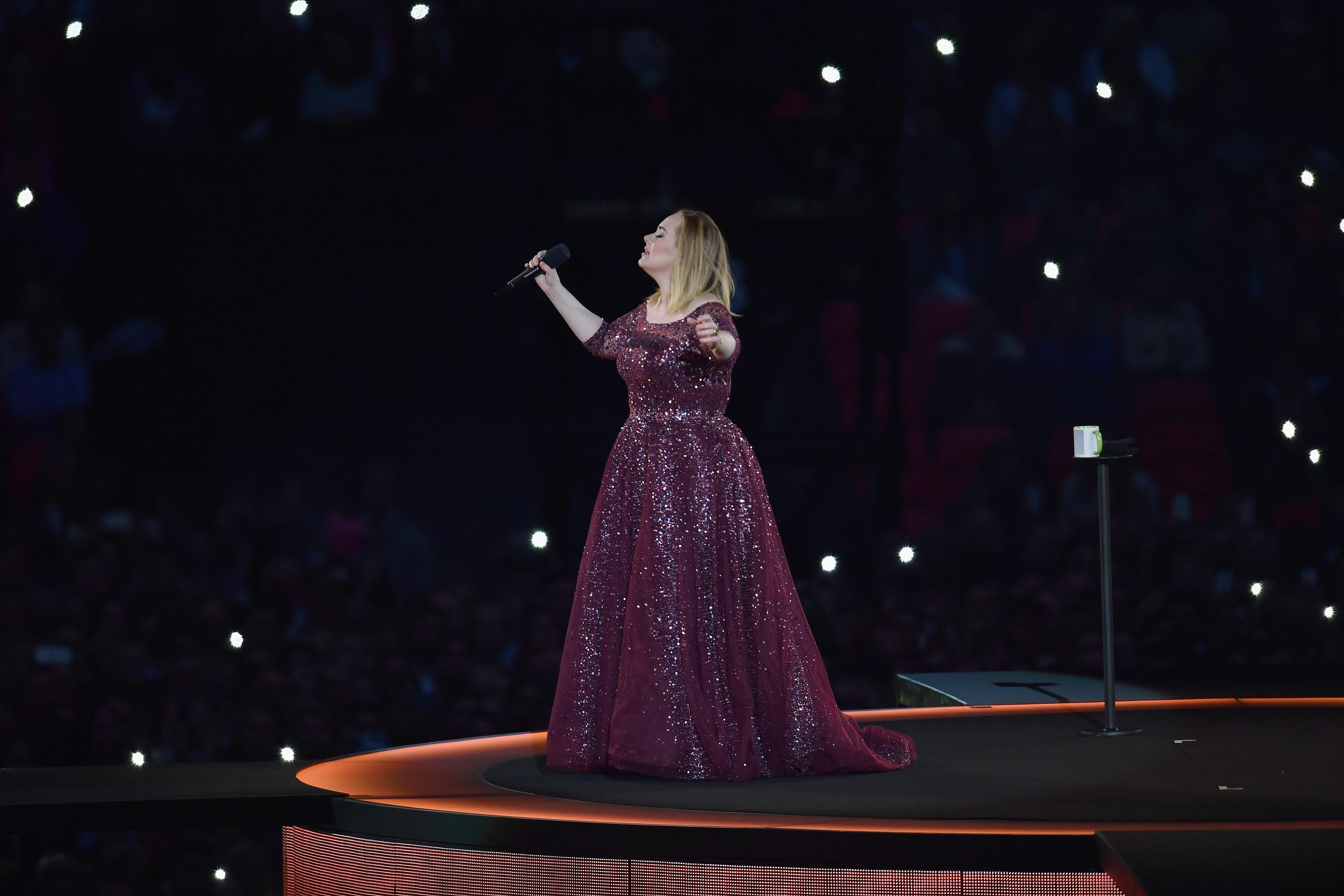 A blonde woman stands on a stage, singing against a black starry backdrop.