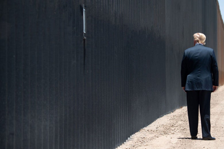 Donald Trump stands beside a wall with his back to the camera.