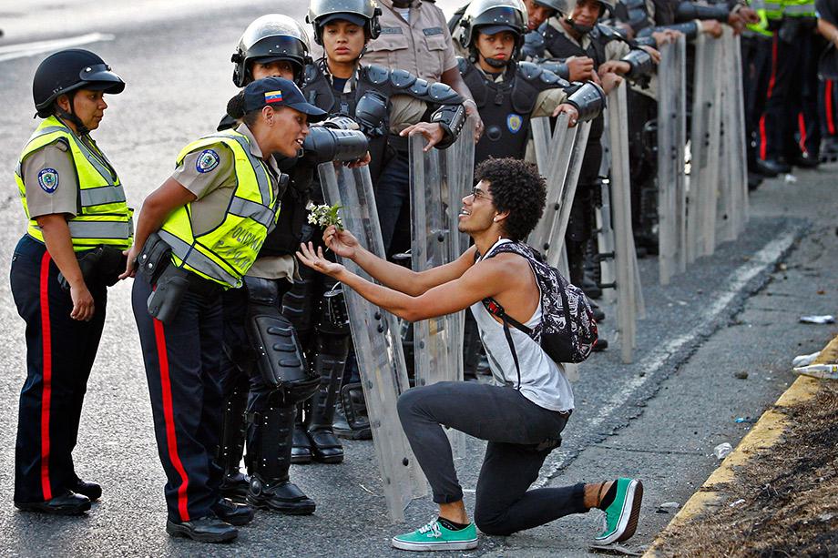 An opposition demonstrator gives flowers to a police officer as demonstrators block the city's main highway during a protest against Nicolas Maduro's government in Caracas.