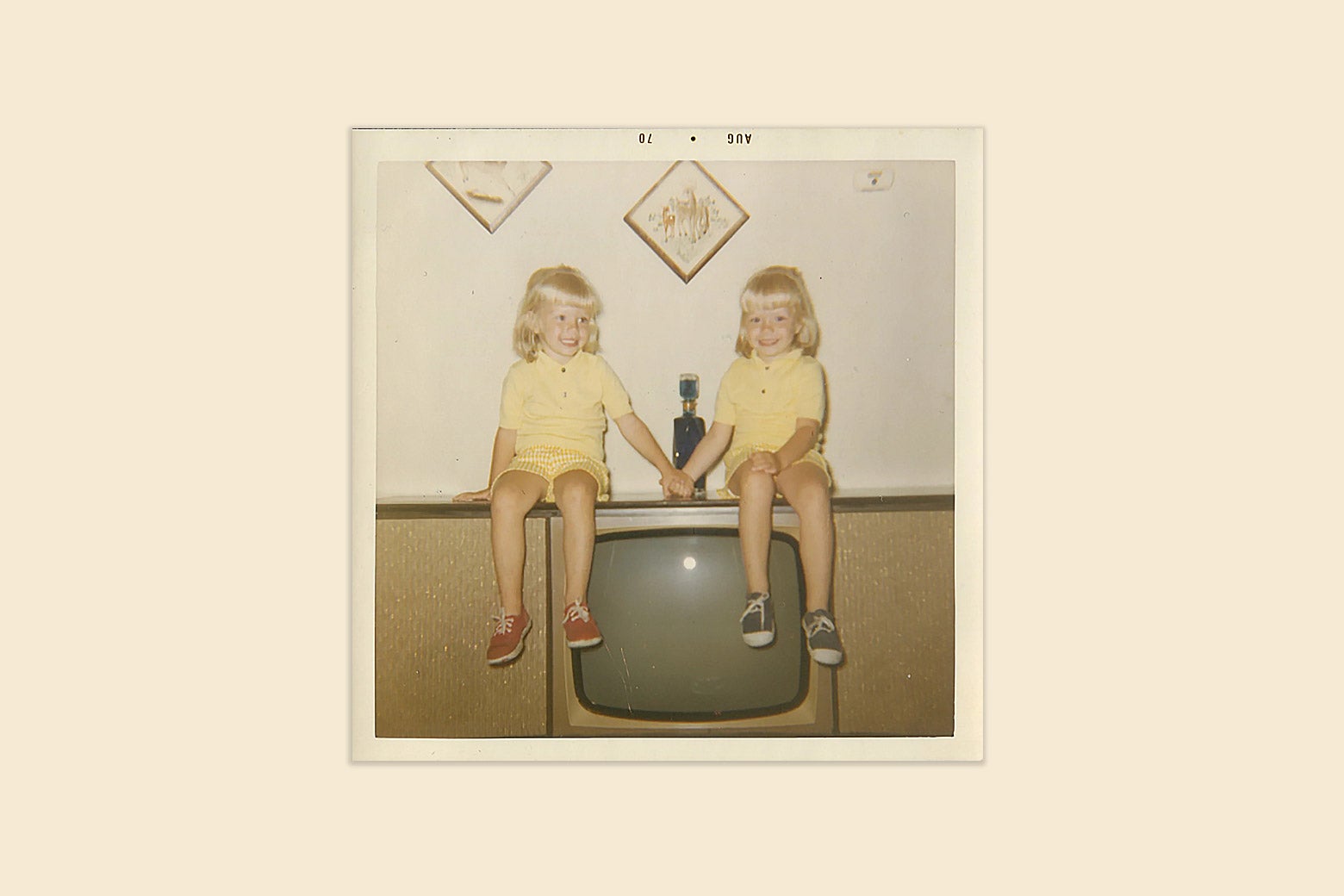 Two blonde girls hold hands on top of a TV set. 