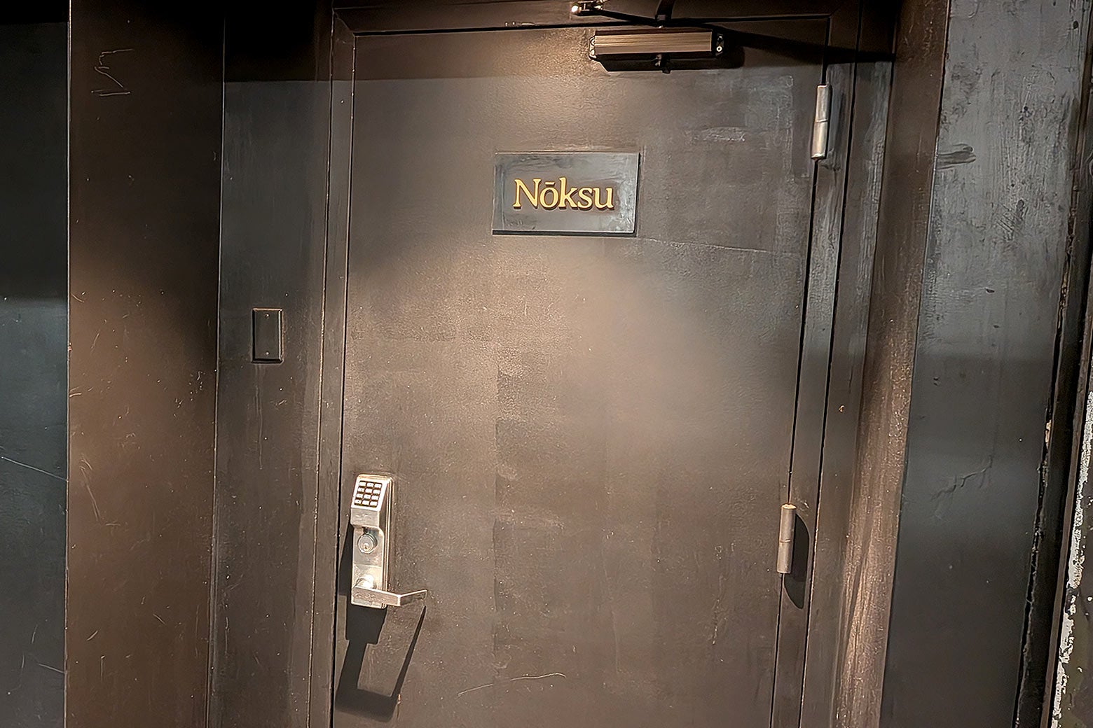 A black door with a key pad entry that says Nōksu on it.