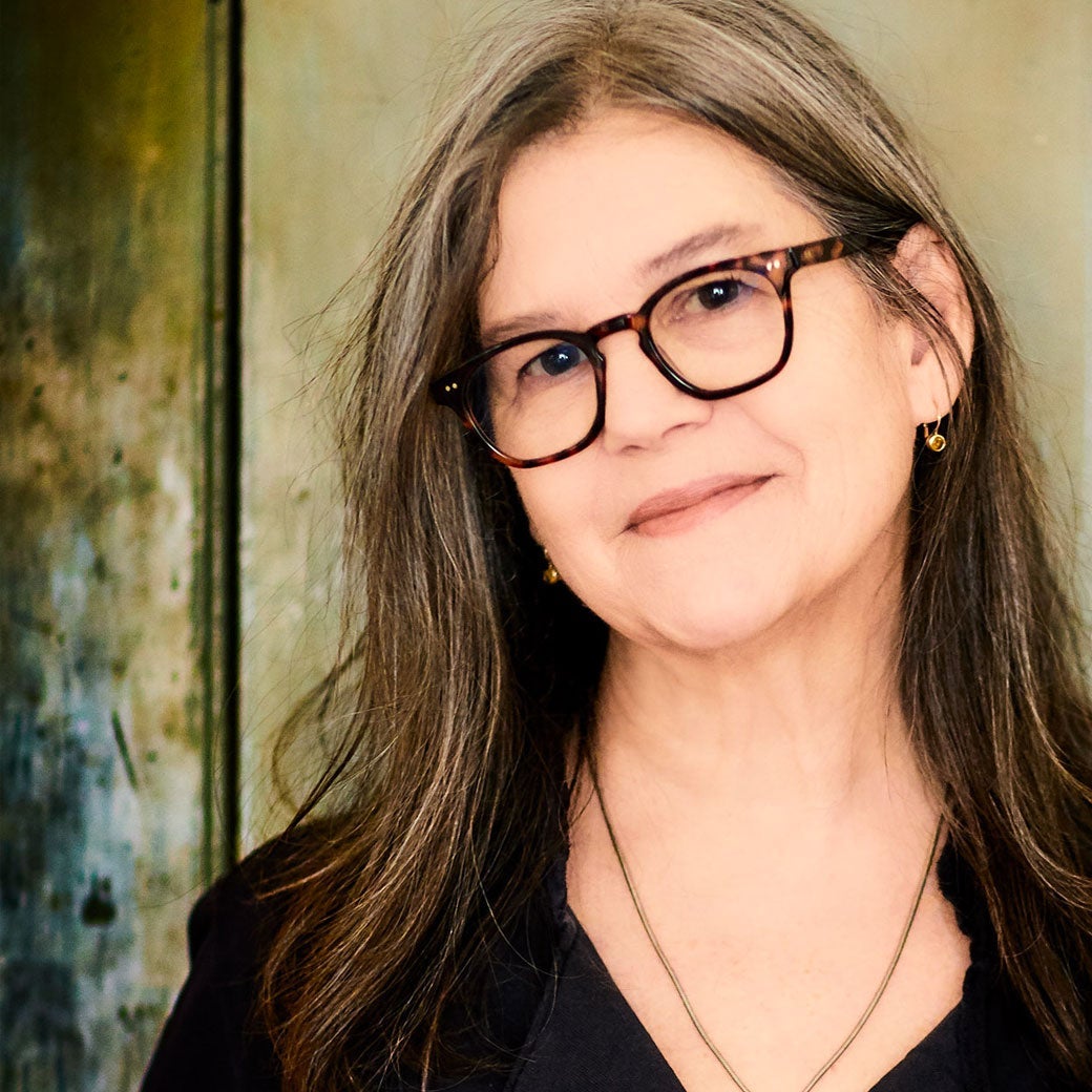 Her long straight hair has streaks of grey and she wears brown thick-rimmed glasses