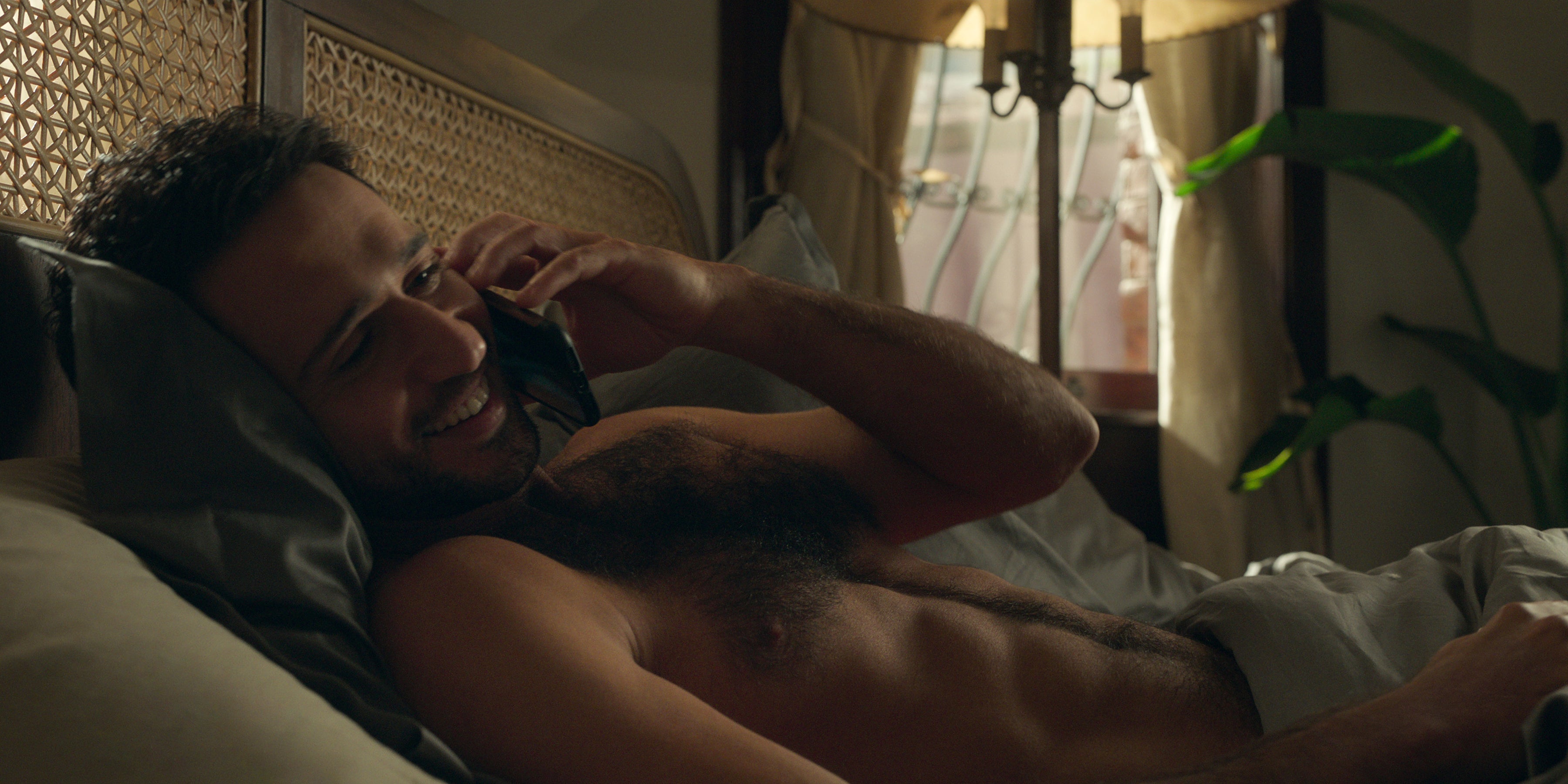 A man in bed talking on the phone.