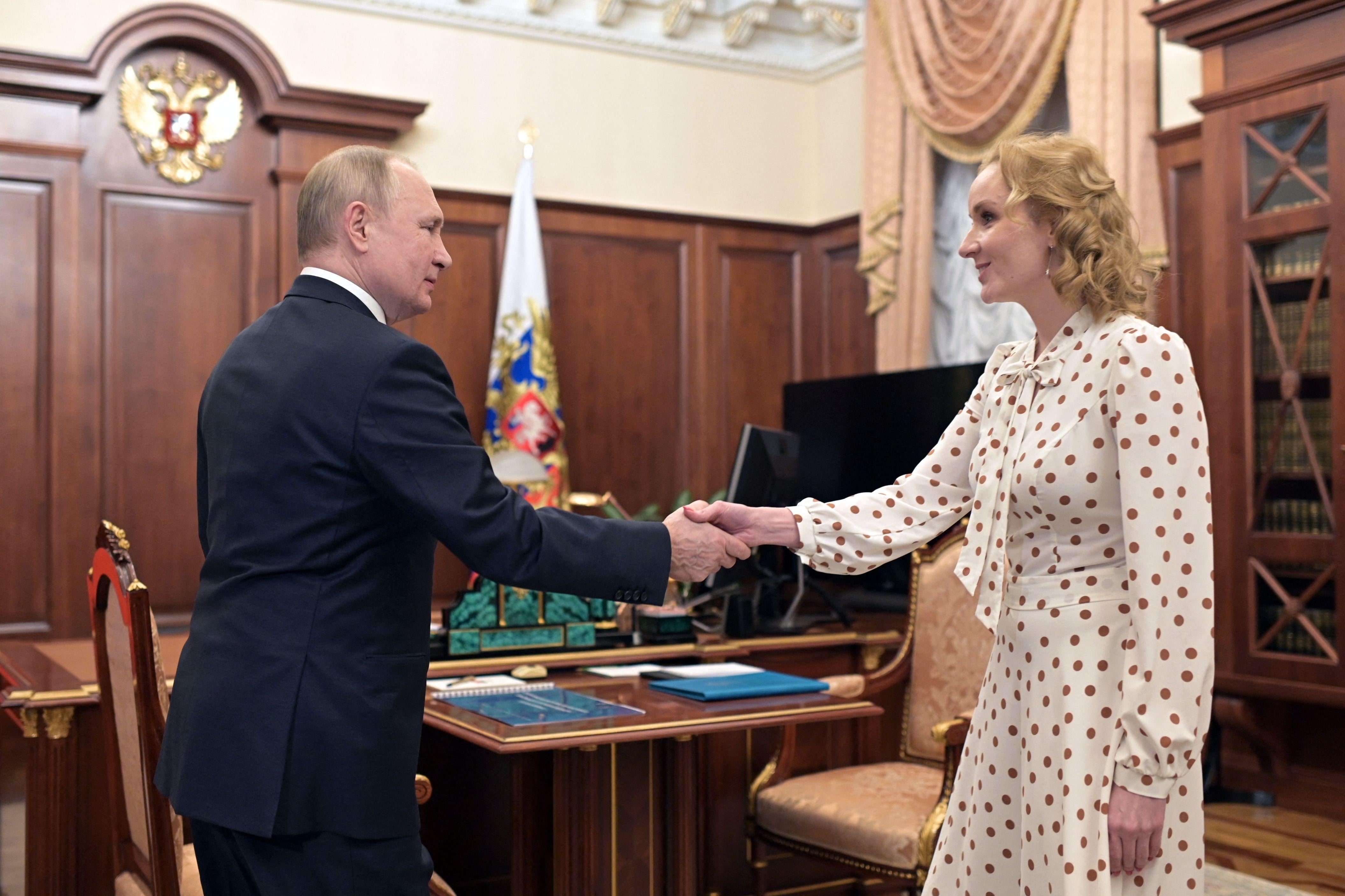 Putin stands far apart from a woman wearing a long dress in front of his desk but does reach out to shake her hand.