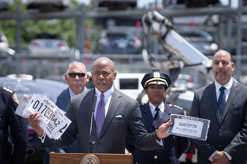 Eric Adams holds up paper license plates while standing in front of other city officials.