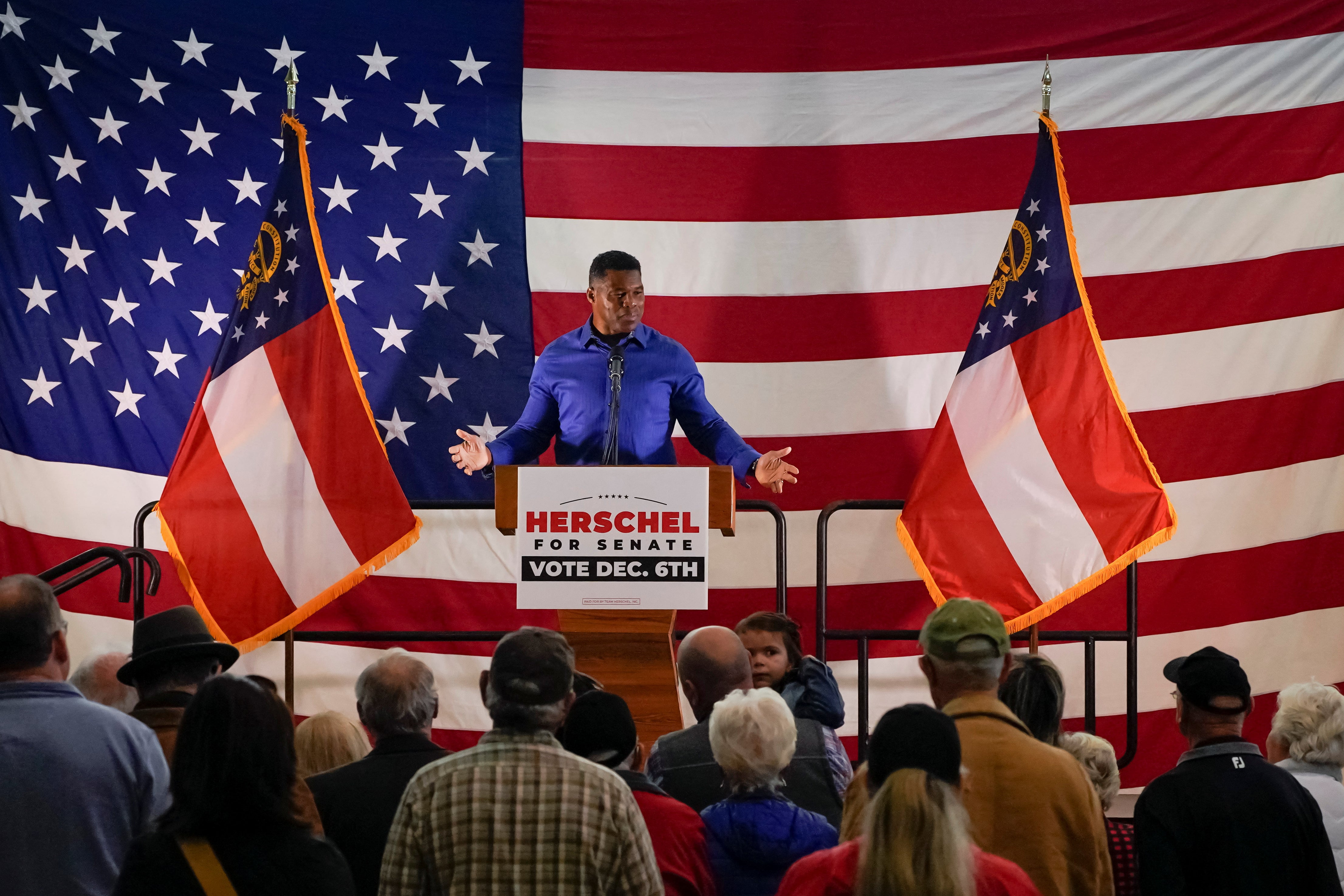 A man addresses a crowd, with an American flag behind him.