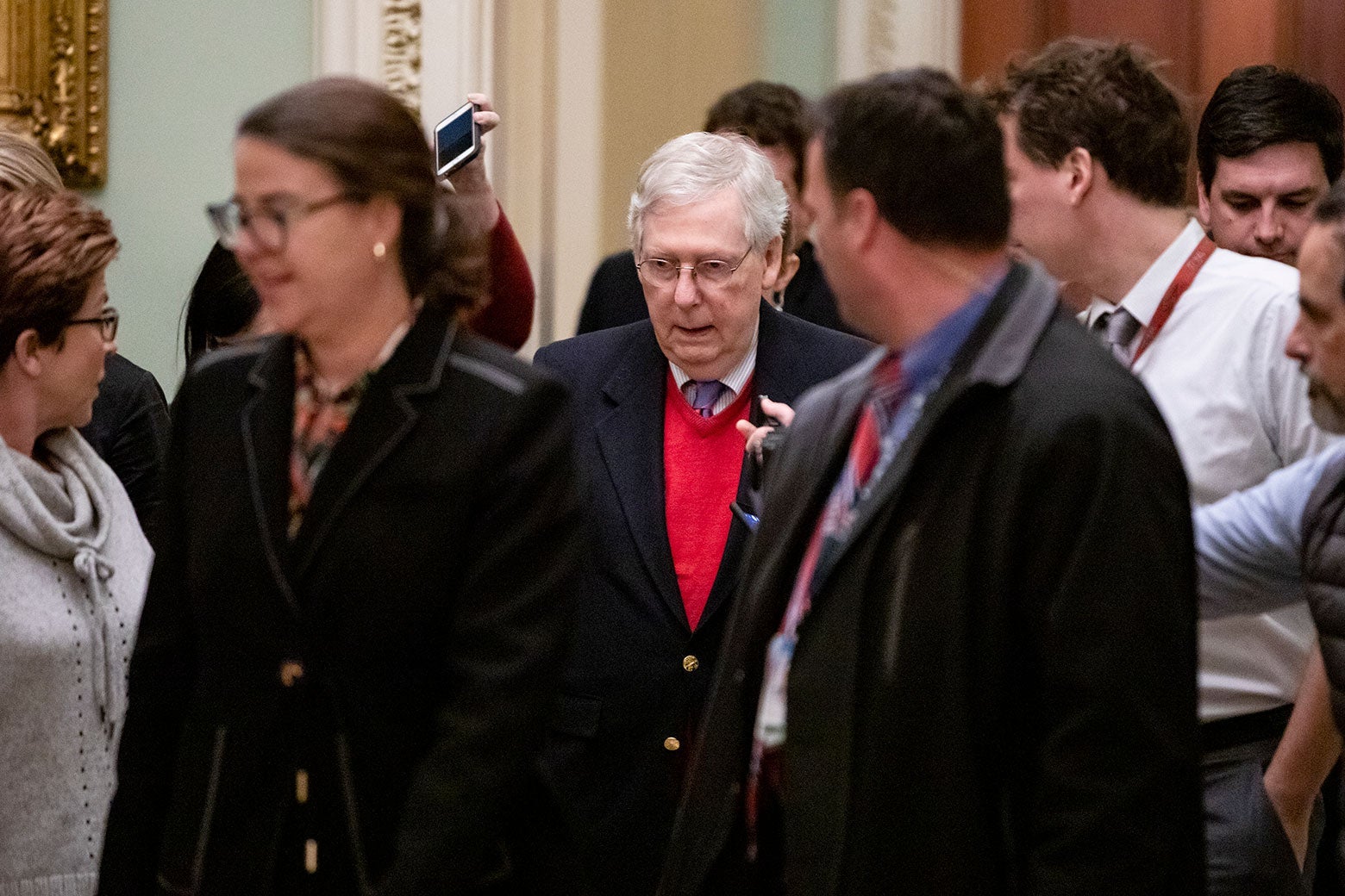 Senate Majority Leader Mitch McConnell is flanked by reporters holding out smartphones and asking him questions.