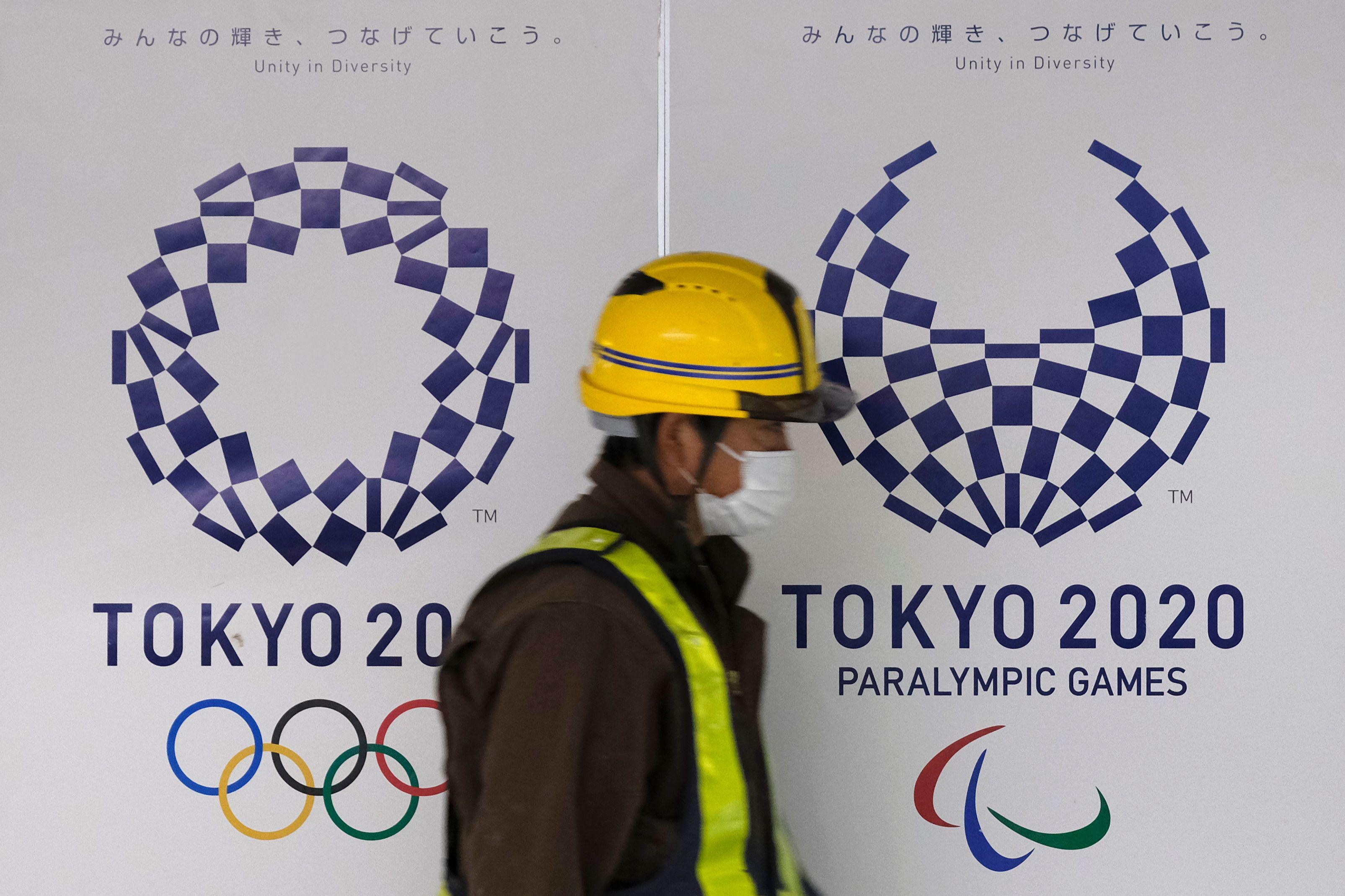 A worker wearing a mask walks by the logo of the Tokyo 2020 Olympic Games and Paralympic Games.