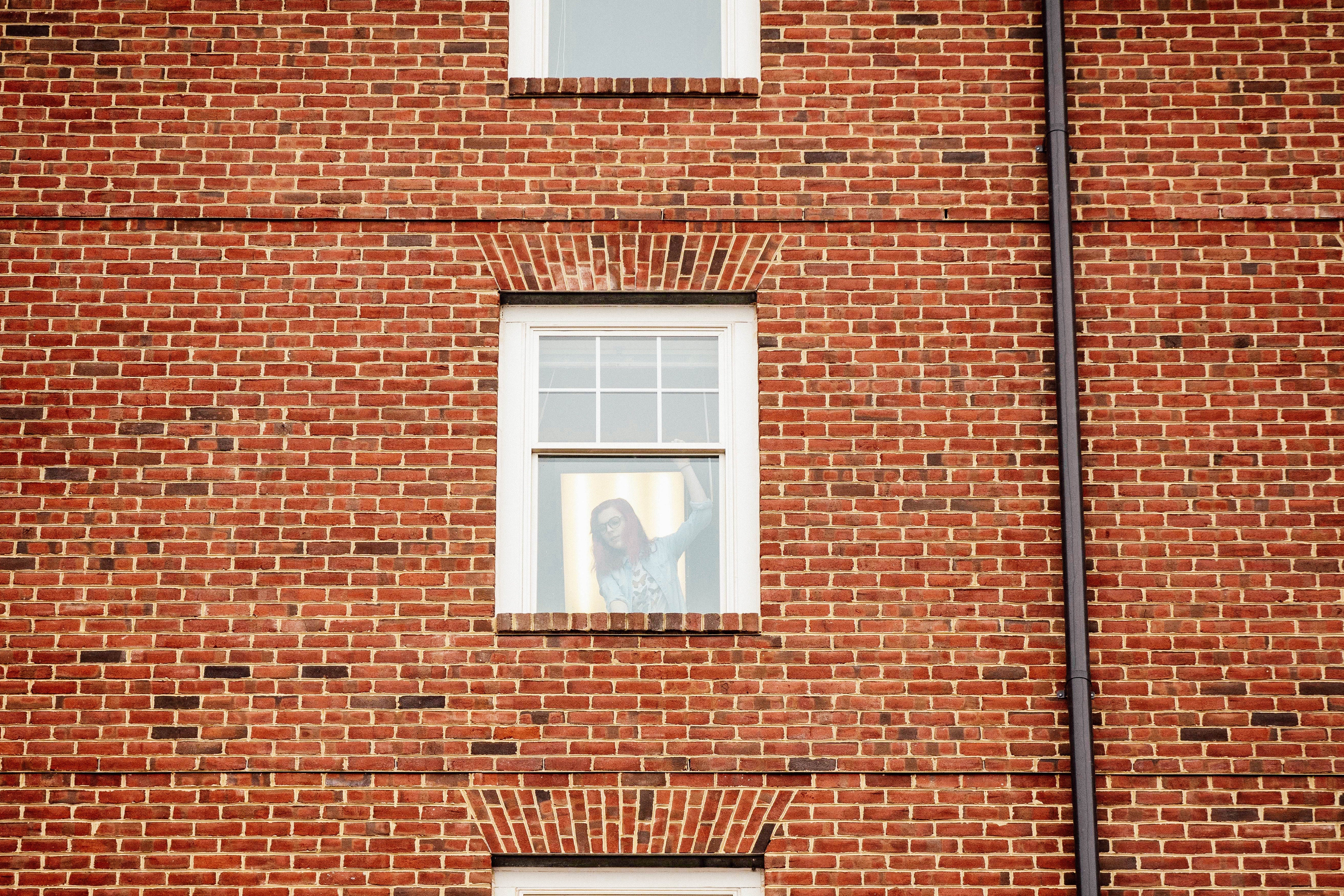 A young woman viewed through her window in a brick building.