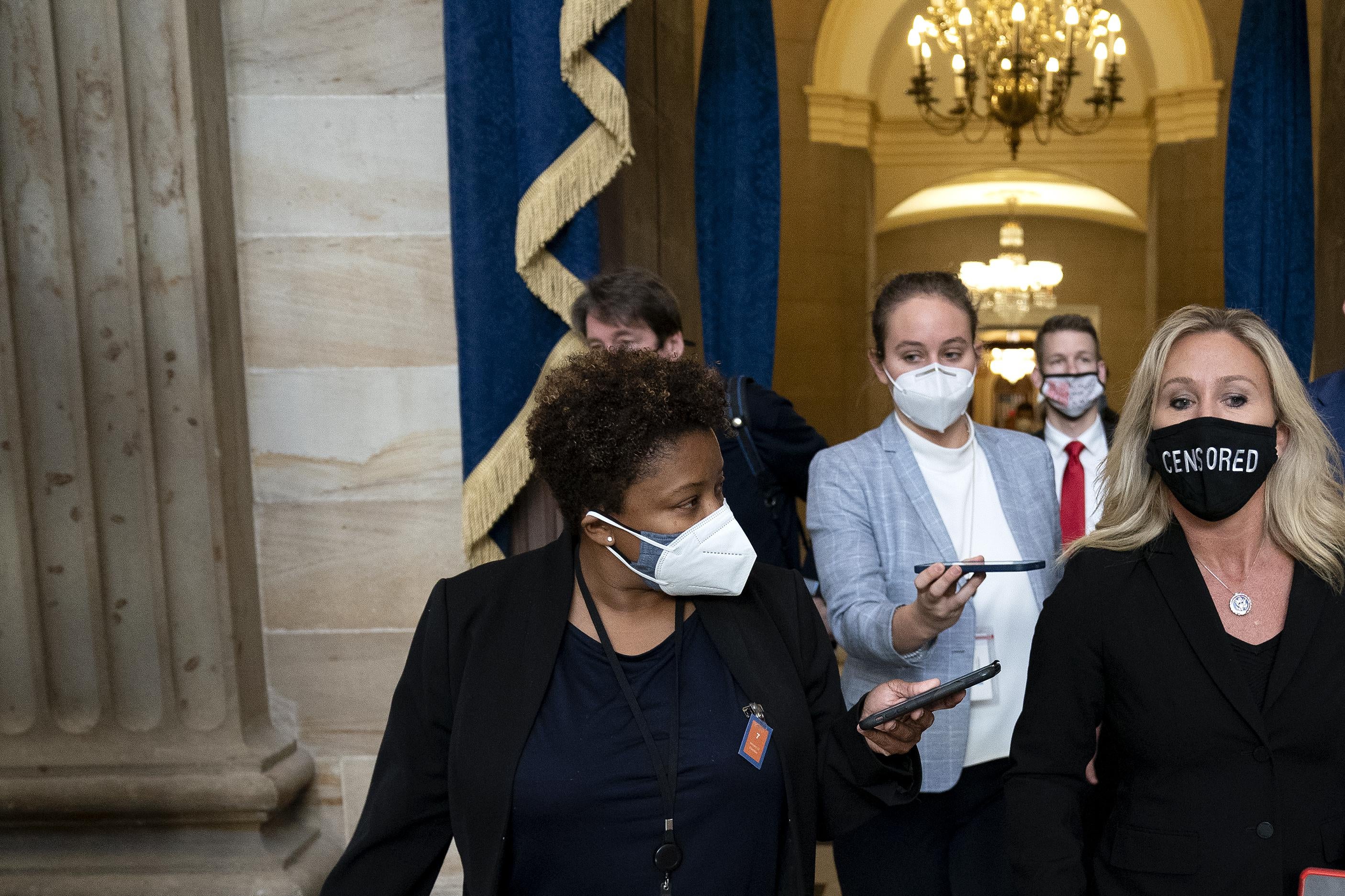 Marjorie Taylor Greene wears a protective mask reading “CENSORED” while walking with others in the Capitol.