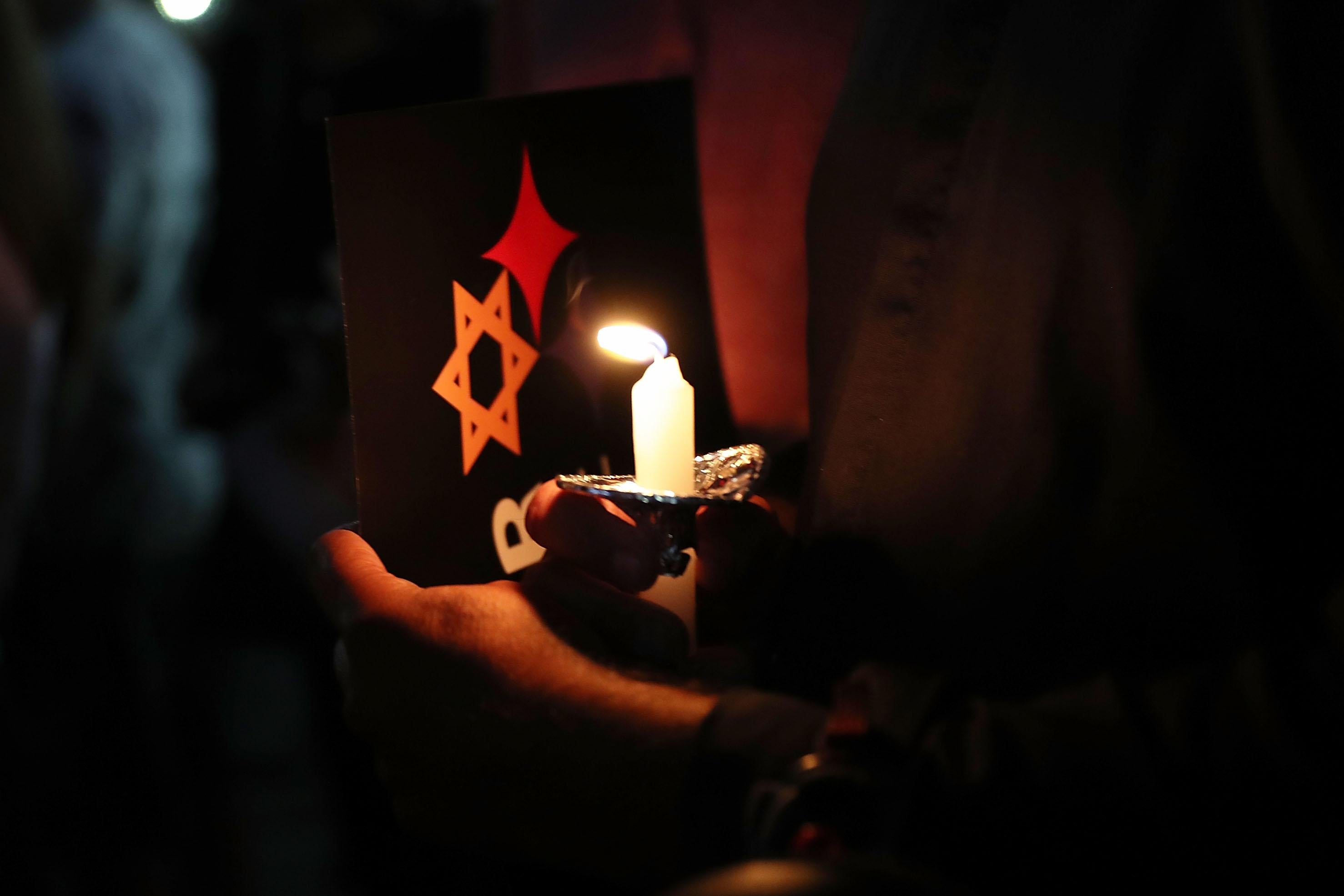 A hand holds a candle and a pamphlet for a solidarity vigil.