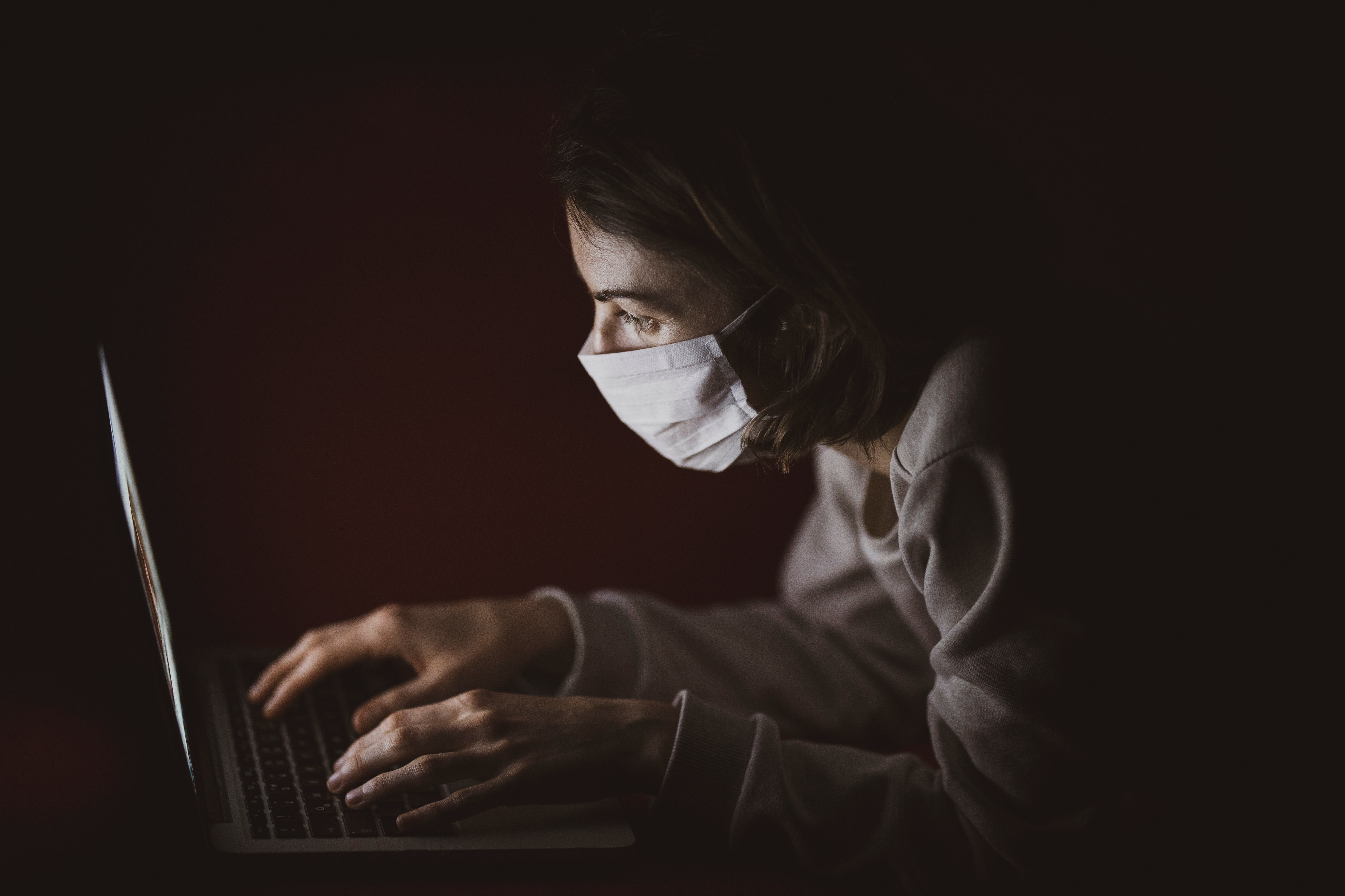 A woman wearing a face mask leans over a laptop.