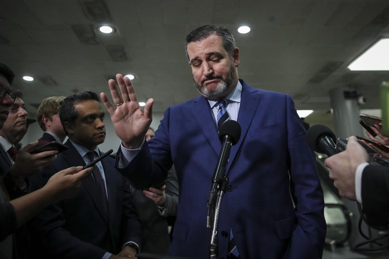 Ted Cruz raises his hand while reporters with microphones surround him.