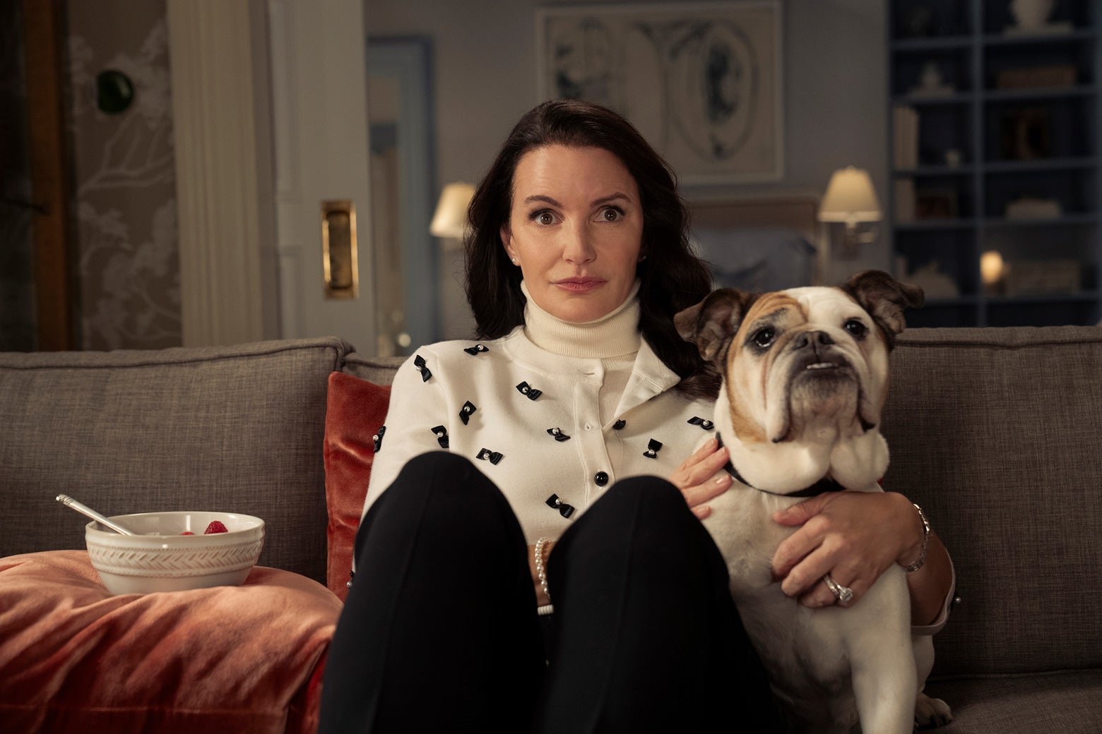 Charlotte sitting on the couch with her bulldog in And Just Like That.