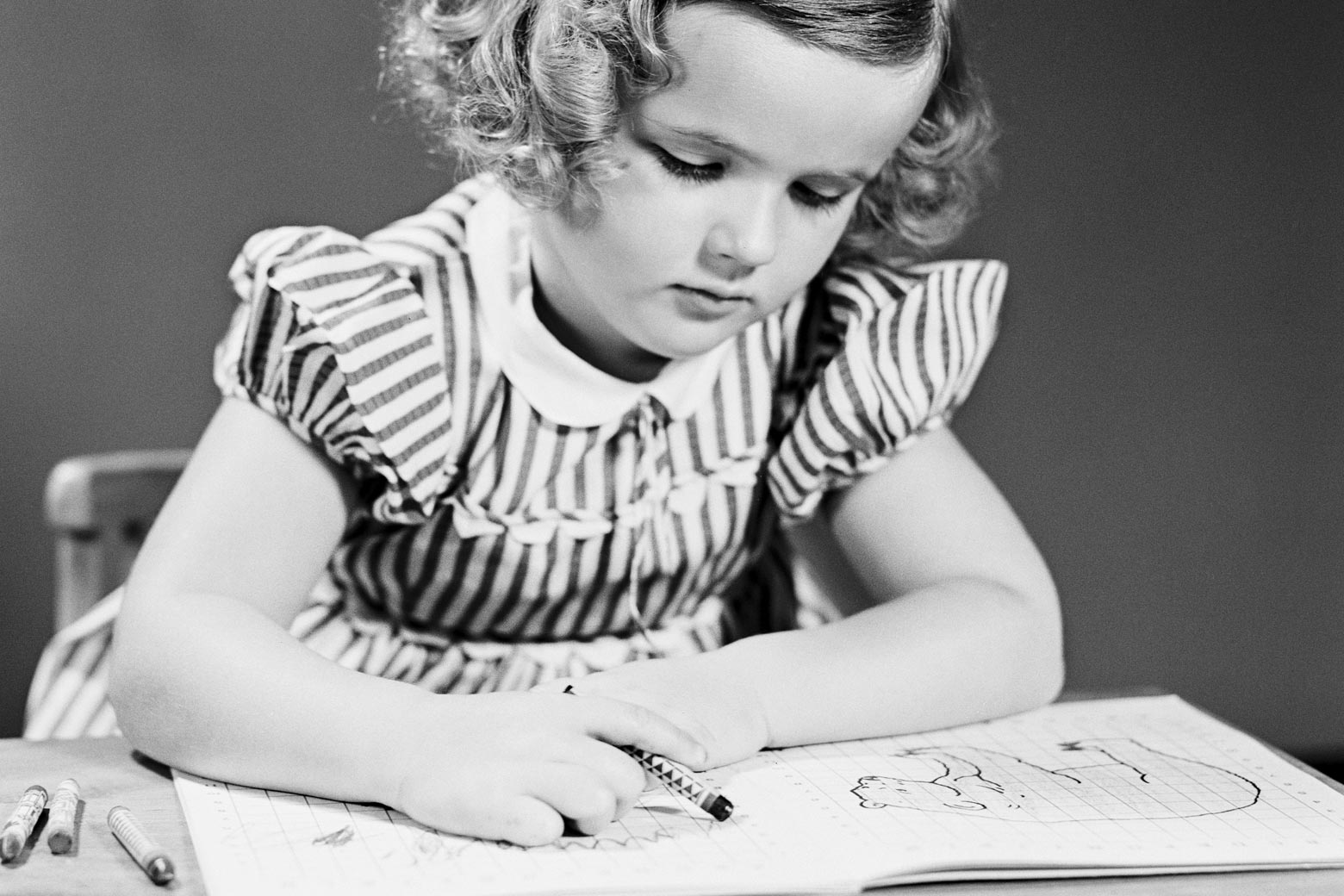 Old black-and-white photo of a little girl coloring in a coloring book