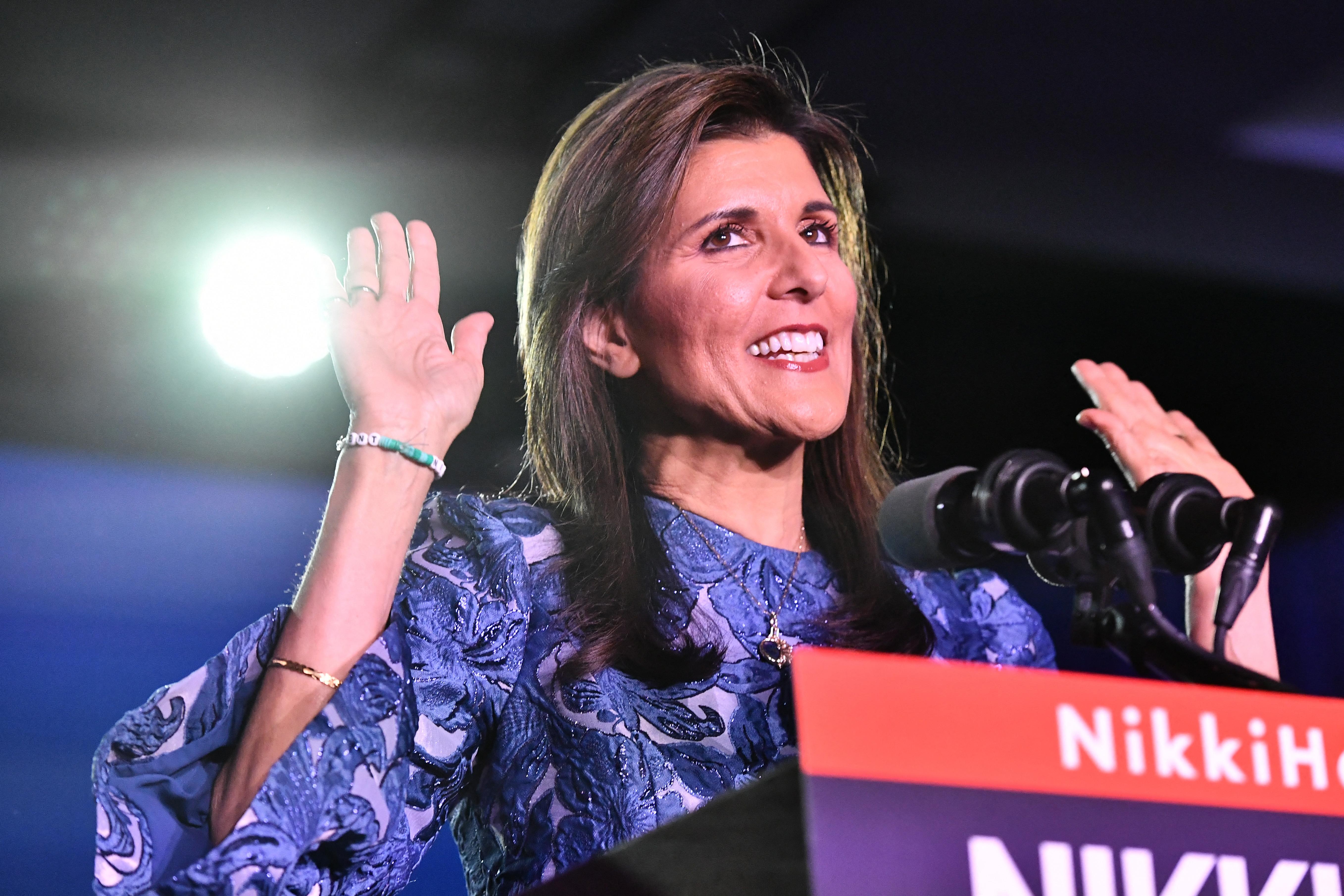 Nikki Haley, onstage at a campaign event, smiles and holds up her hands.