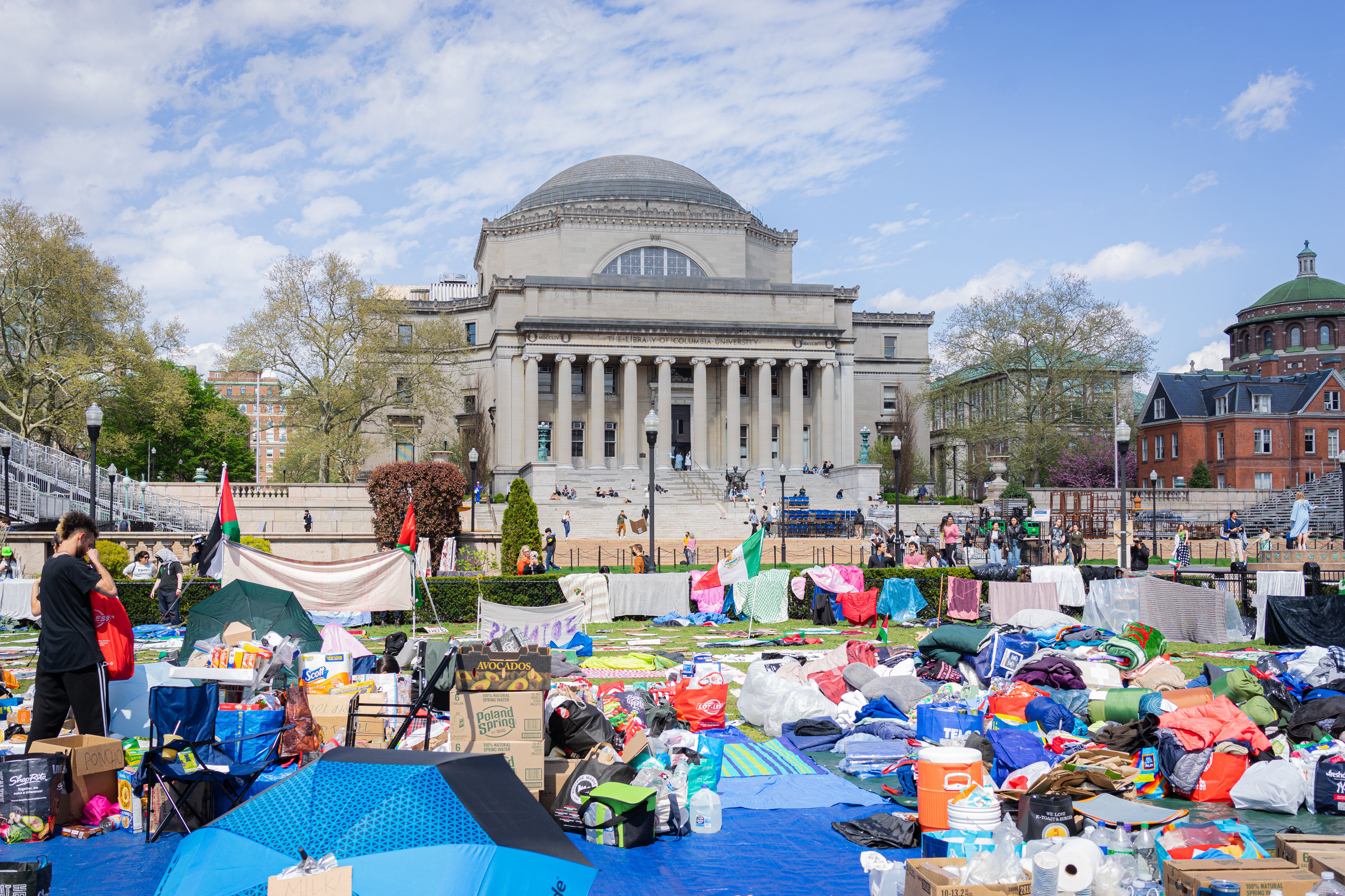A lawn full of tarps and snacks and umbrellas, in front of a stately neoclassical building.