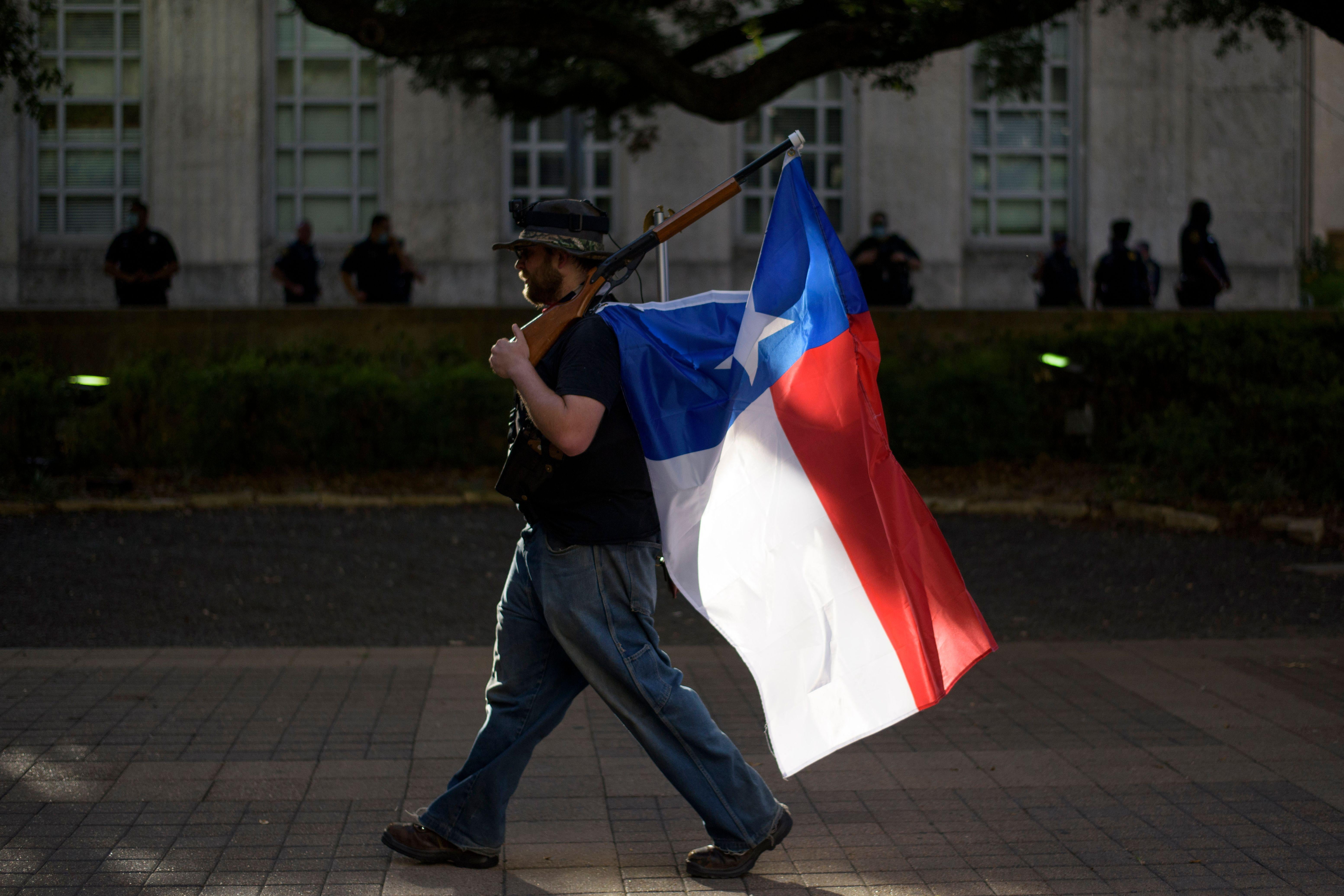 A man walks with a rifle with a Texas flag attached to it during a Police Appreciation rally at the City Hall in Houston.