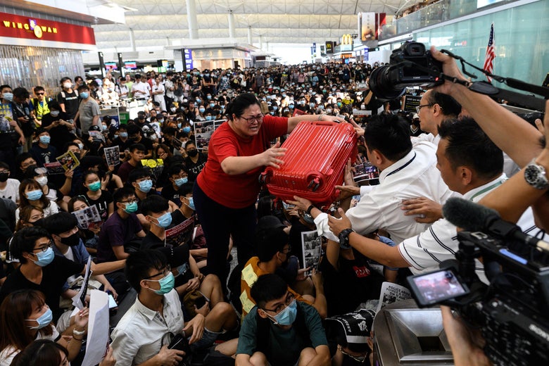 A tourist passes her luggage to security guards amid a crowd of masked people protesting in the airport.