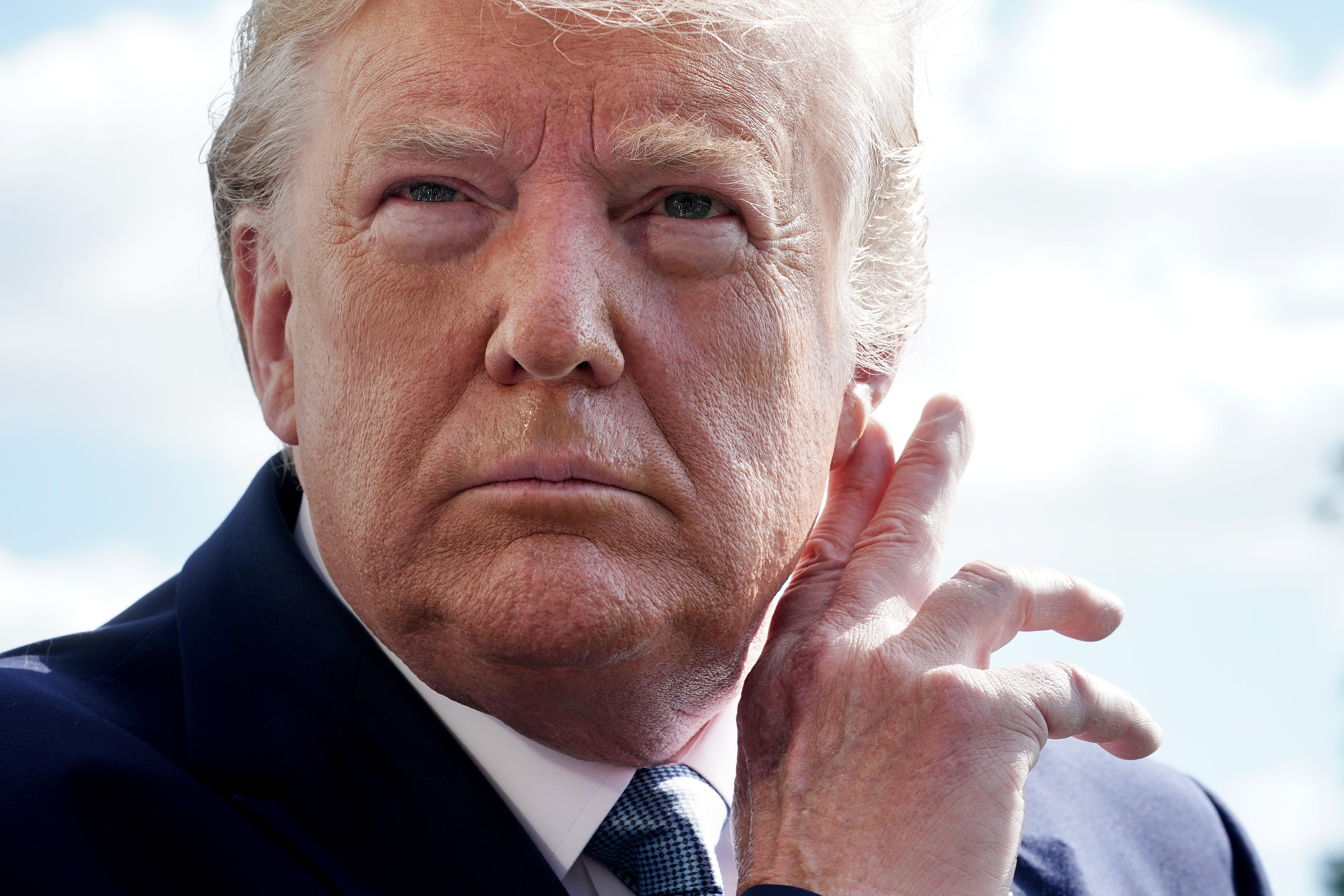 Trump holds his fingers to his ear in a gesture to hear better.