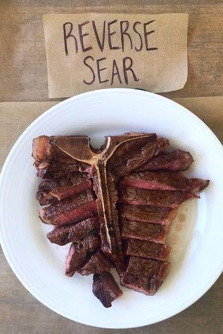 A T-bone steak on a plate next to a sign labelled "Reverse Sear."