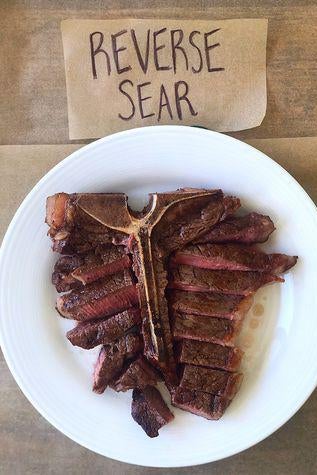 A T-bone steak on a plate next to a sign labelled "Reverse Sear."