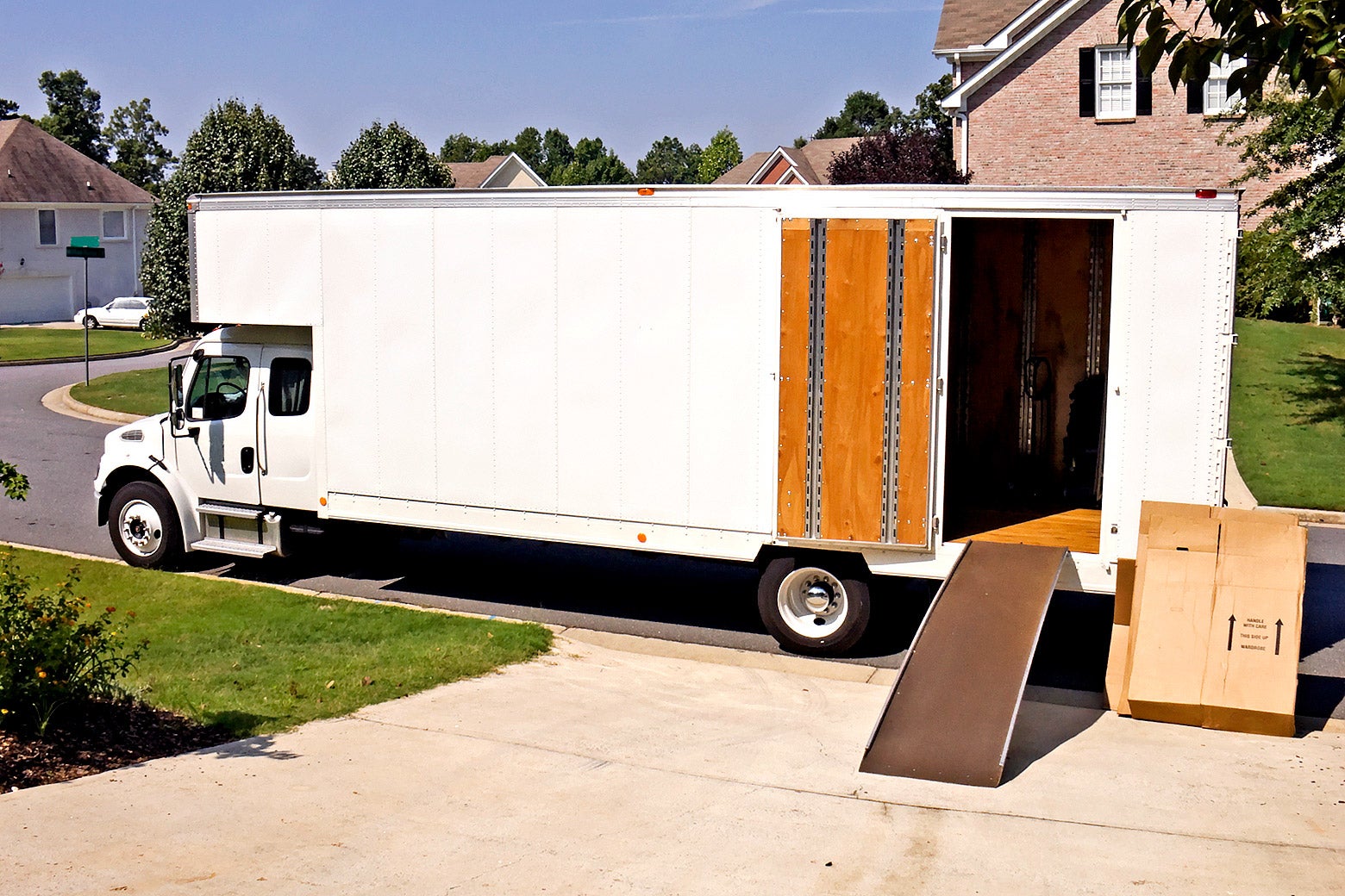 An image of a moving van with door open, ramp down, and boxes nearby. 
