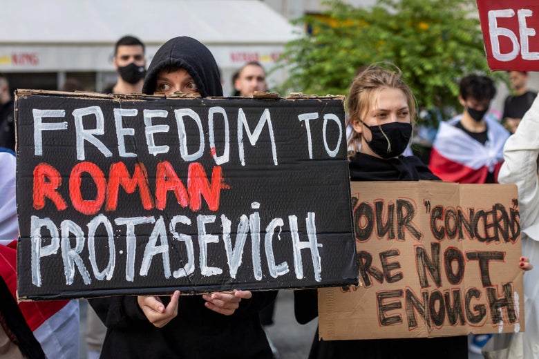 One person holds up a sign that says "Freedom to Roman Protasevich" next to a person holding a sign that says "Your concerns are not enough."