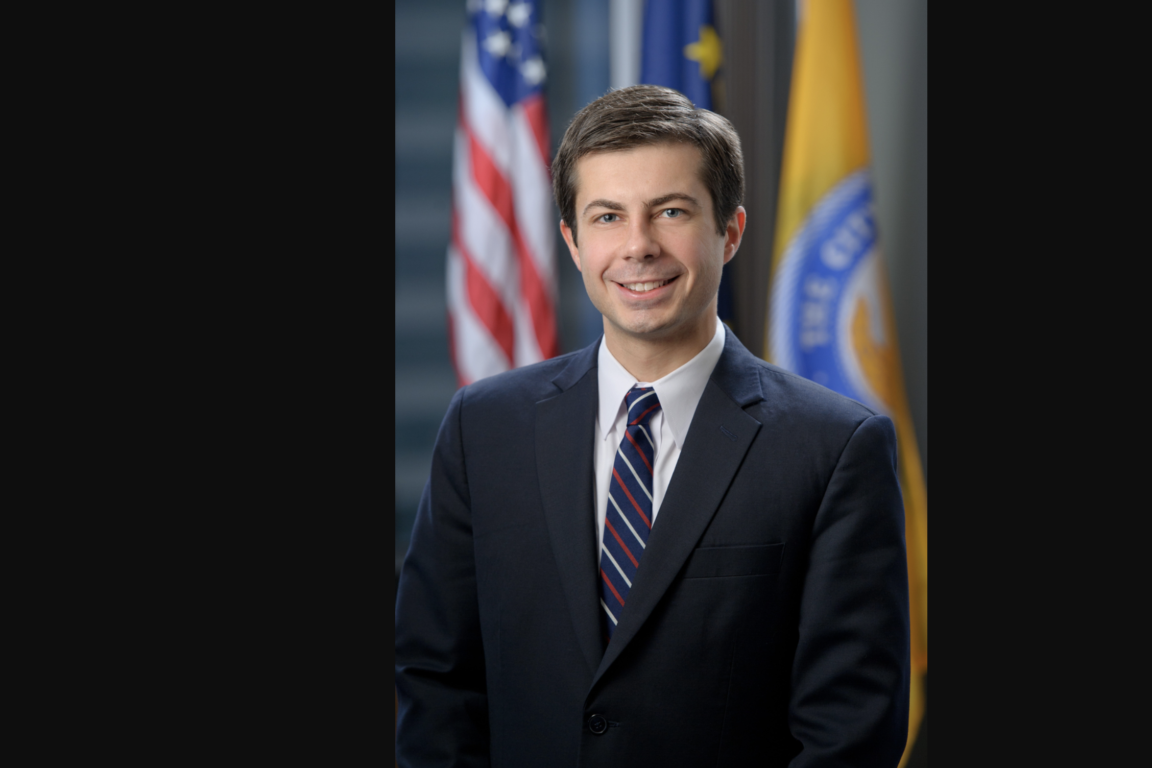 Pete Buttigieg smiling in front of an American flag and an Indiana flag in his official 2012 portrait.