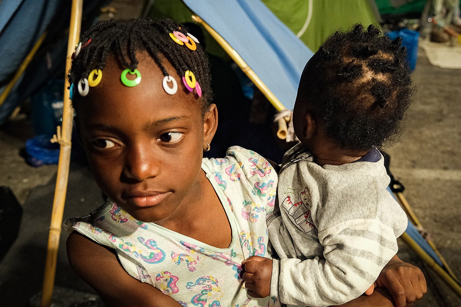 A girl with beads in her hair holds a baby.