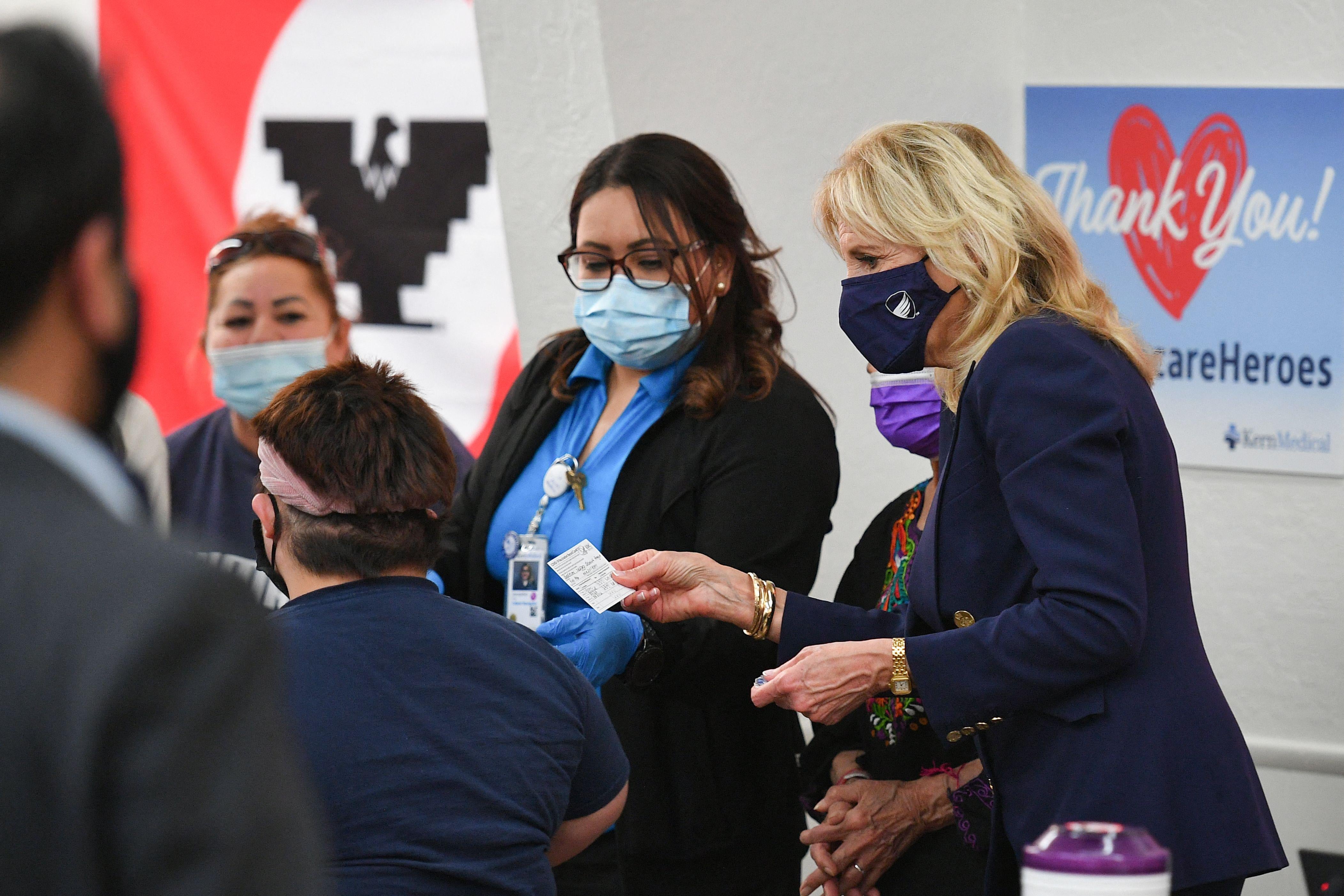 Masked health care workers standing next to Jill Biden, who holds a vaccination card.