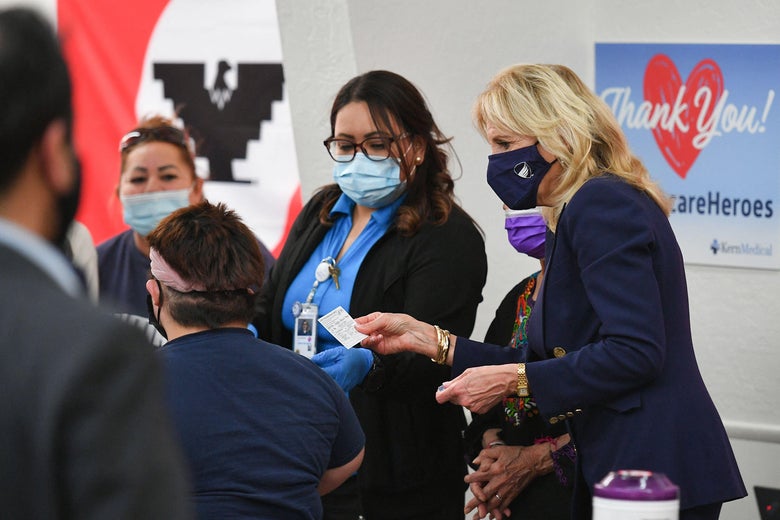 Masked health care workers standing next to Jill Biden, who holds a vaccination card.