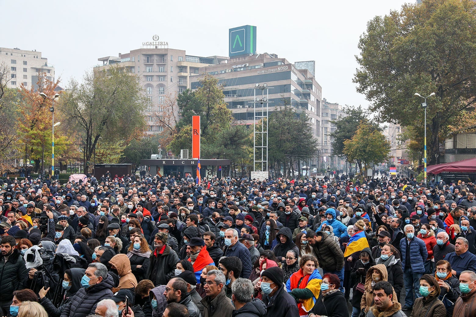 A crowd of people, mostly wearing masks, in an urban center.