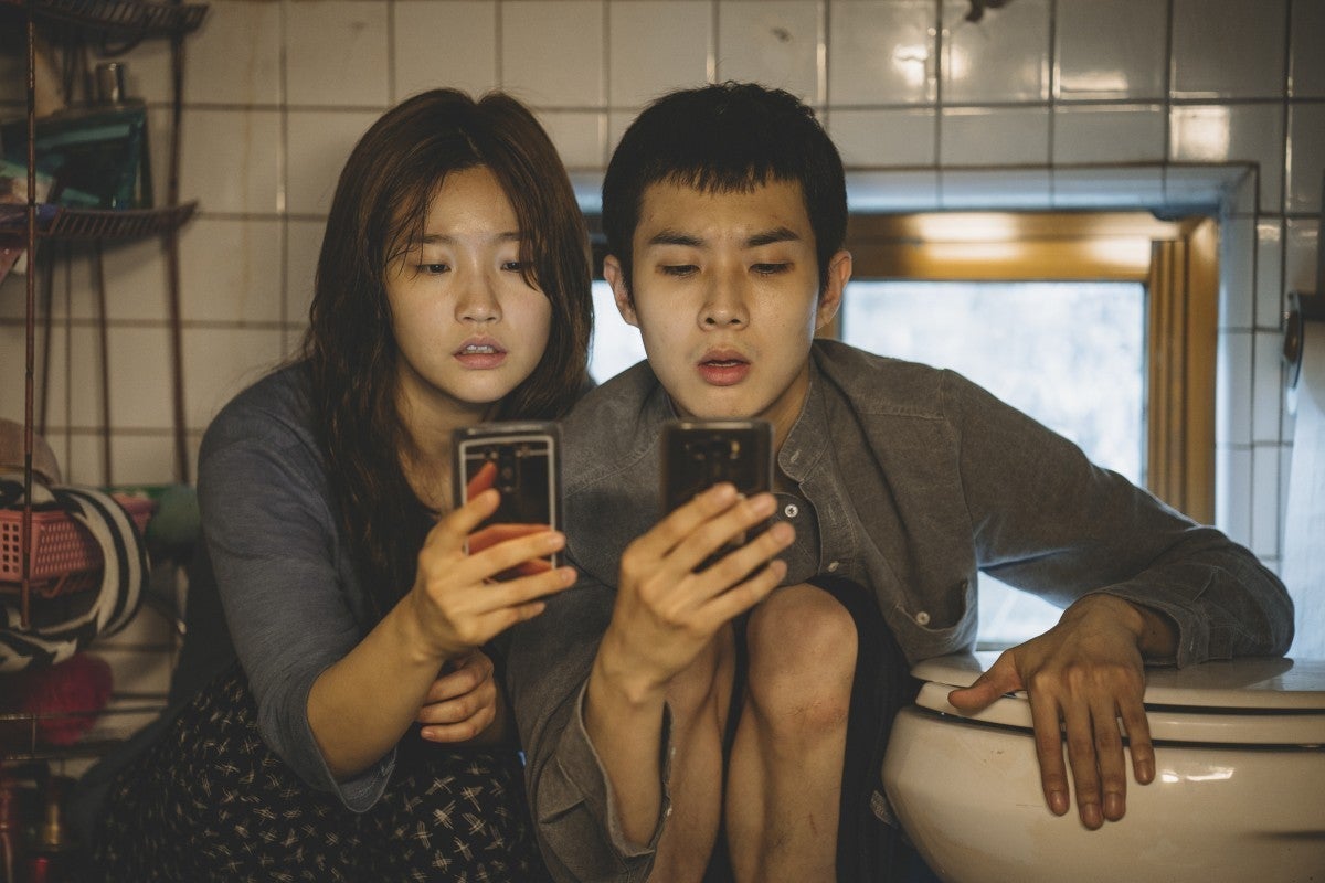 Park So-dam and Choi Woo-shik crouch next to a toilet, looking at their phones.