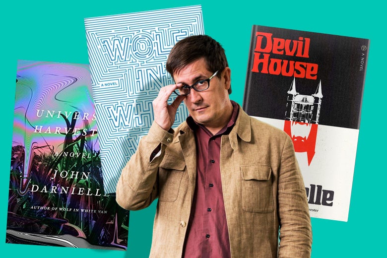 John Darnielle is seen adjusting his glasses in front of the covers of his three novels.