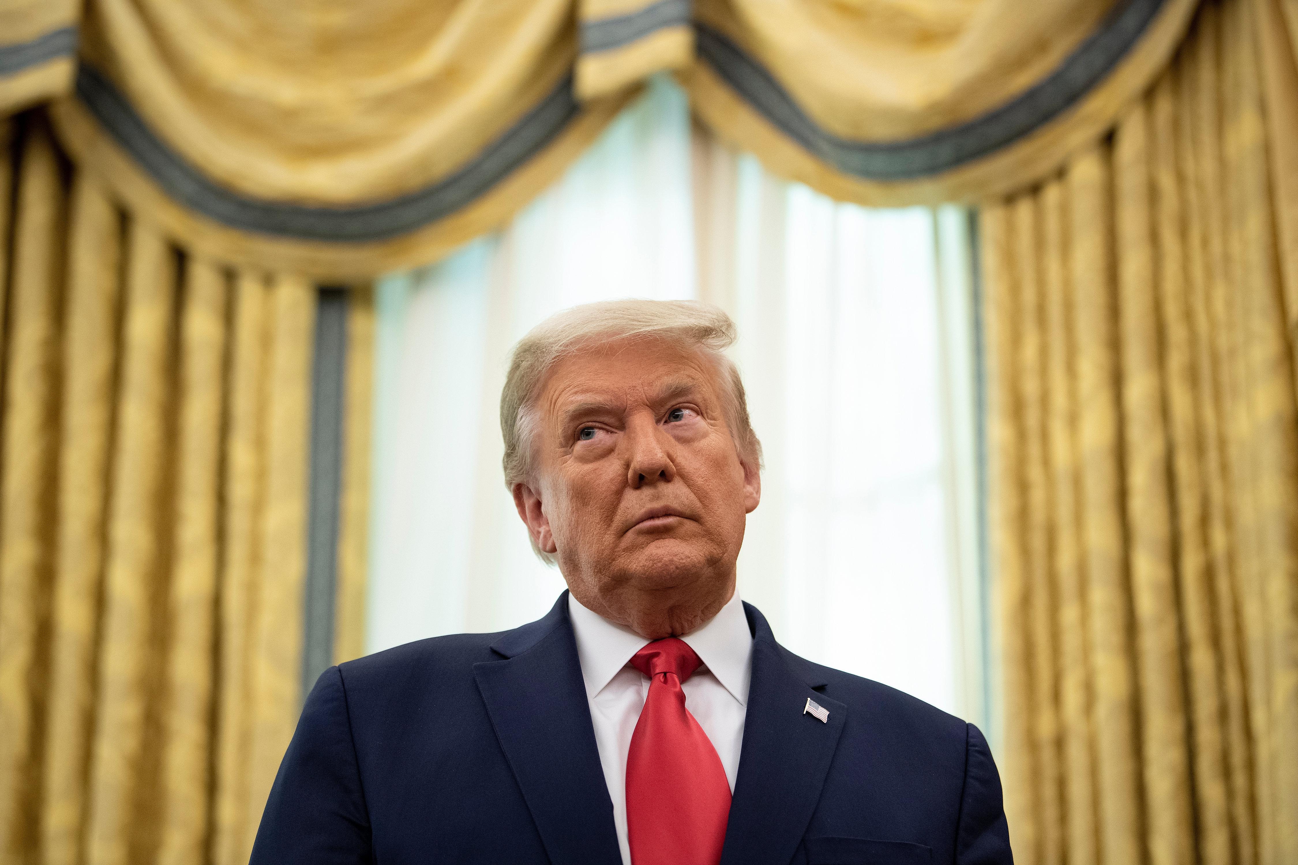 Donald Trump, standing, leans his head to the side and glances upward