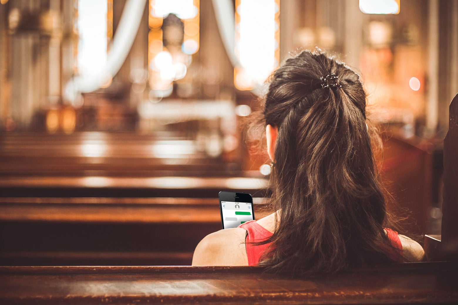 A worshipper stares at their phone while sitting in a church pew.