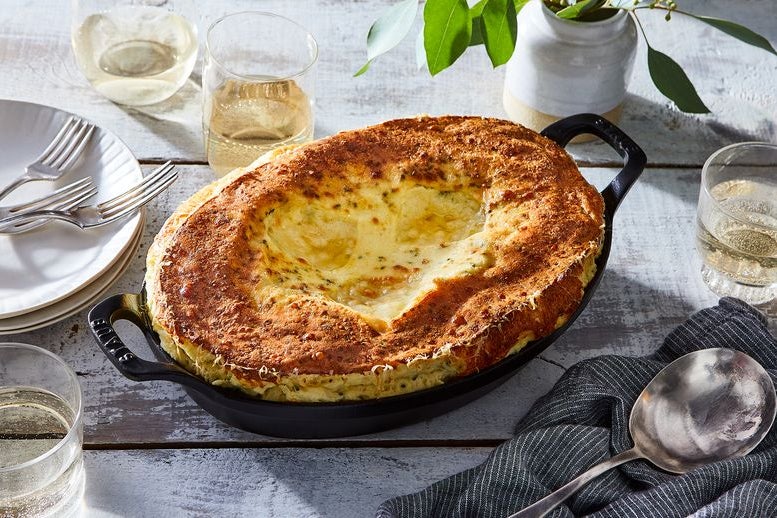 A yellow soufflé inside an oval cast-iron gratin pan.