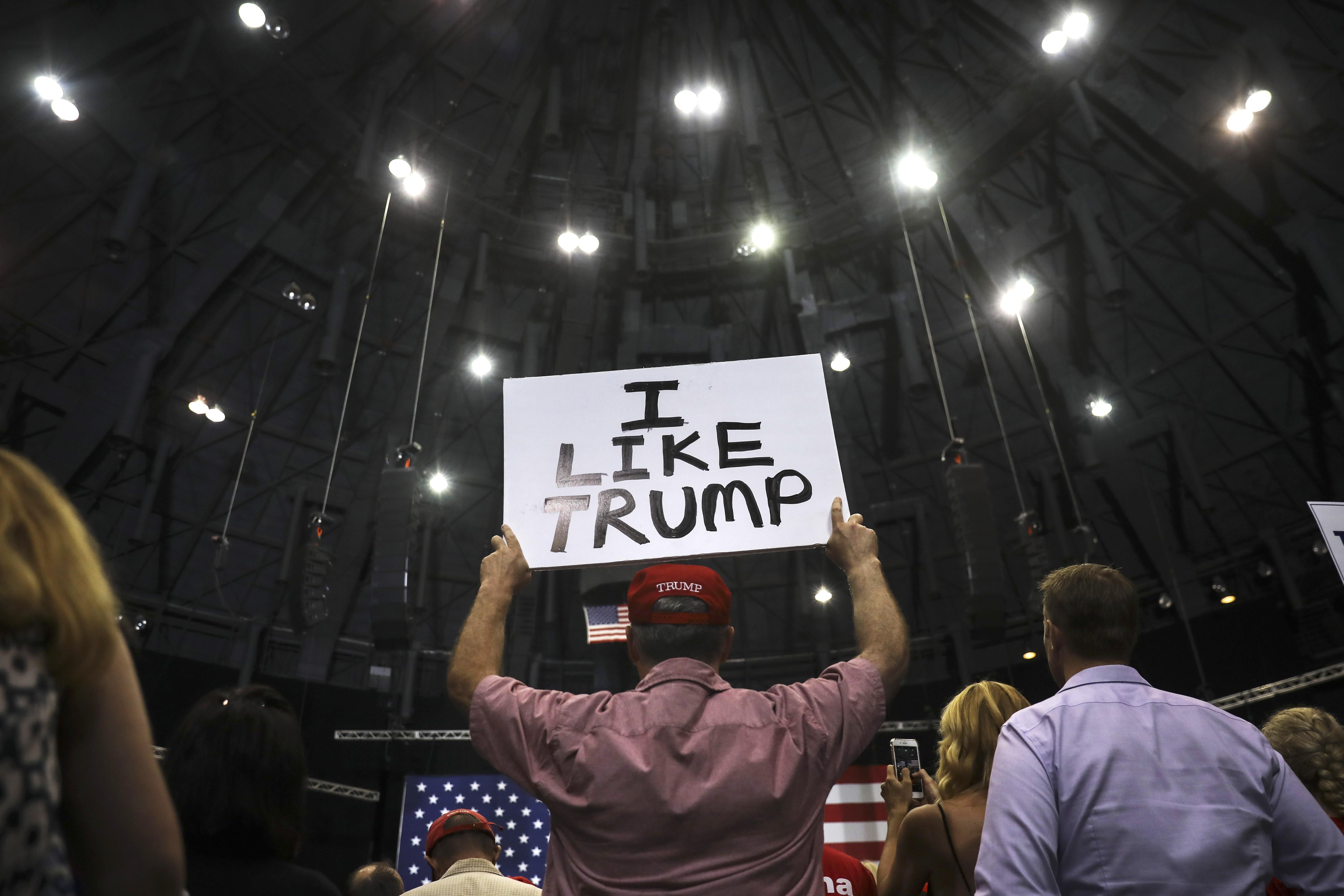 A supporter in a red Trump hat holds up a sign that says, "I like Trump."
