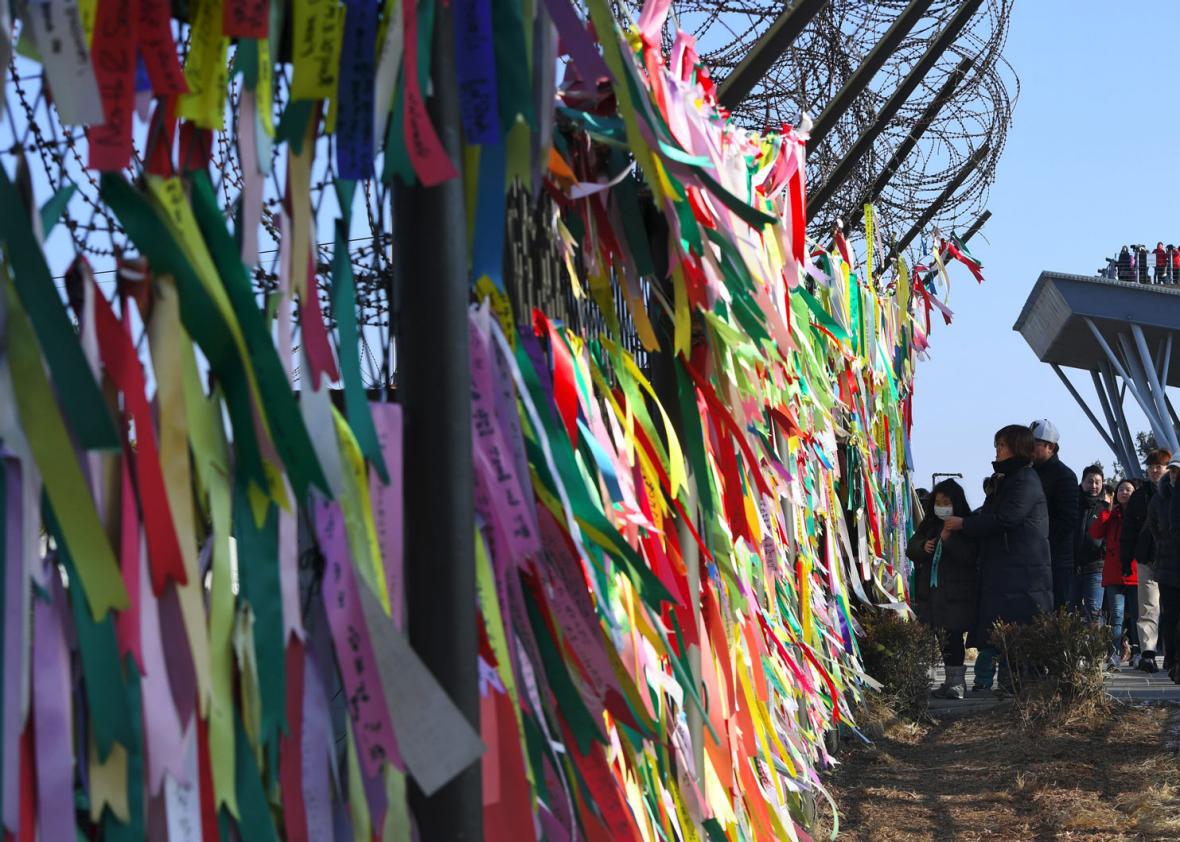 People look at ribbons with inscriptions calling for peace and reunification displayed on a military fence at the Imjingak peace park