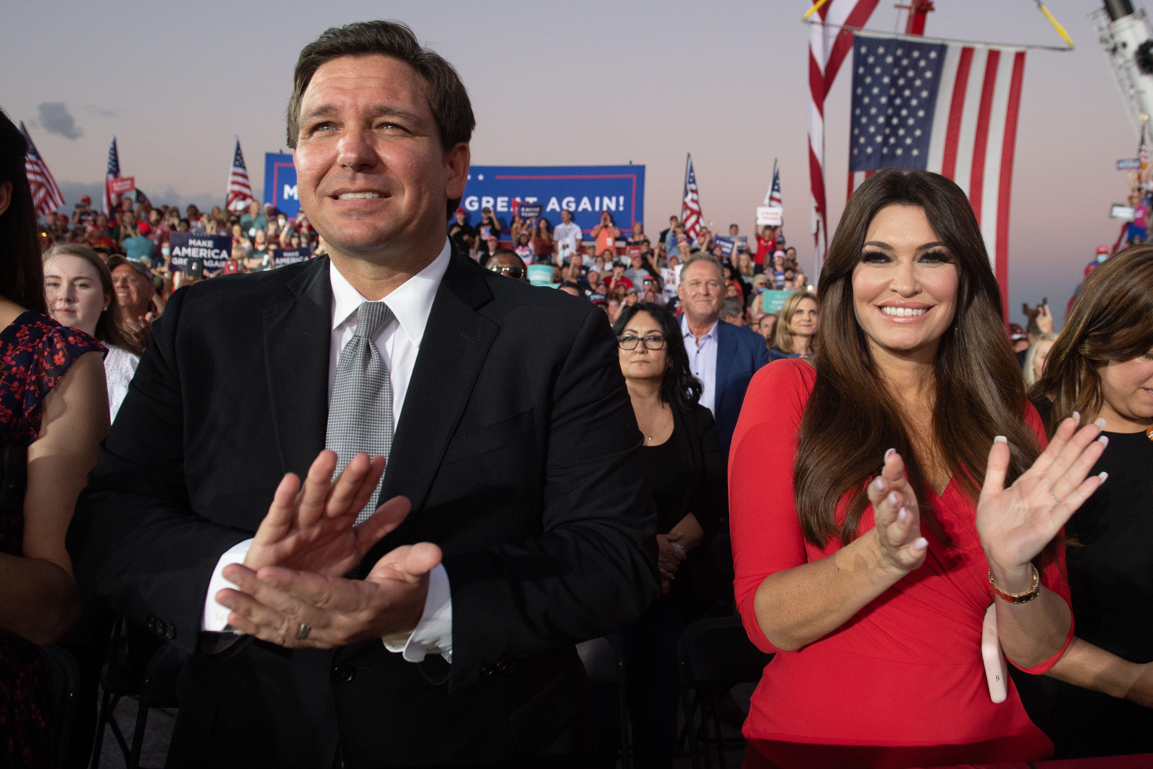 Florida Governor Ron DeSantis (L) and Kimberly Guilfoyle (R), finance chair of US President Donald Trump's campaign, applaud as Trump holds a Make America Great Again rally as he campaigns at Orlando Sanford International Airport in Sanford, Florida, October 12, 2020.